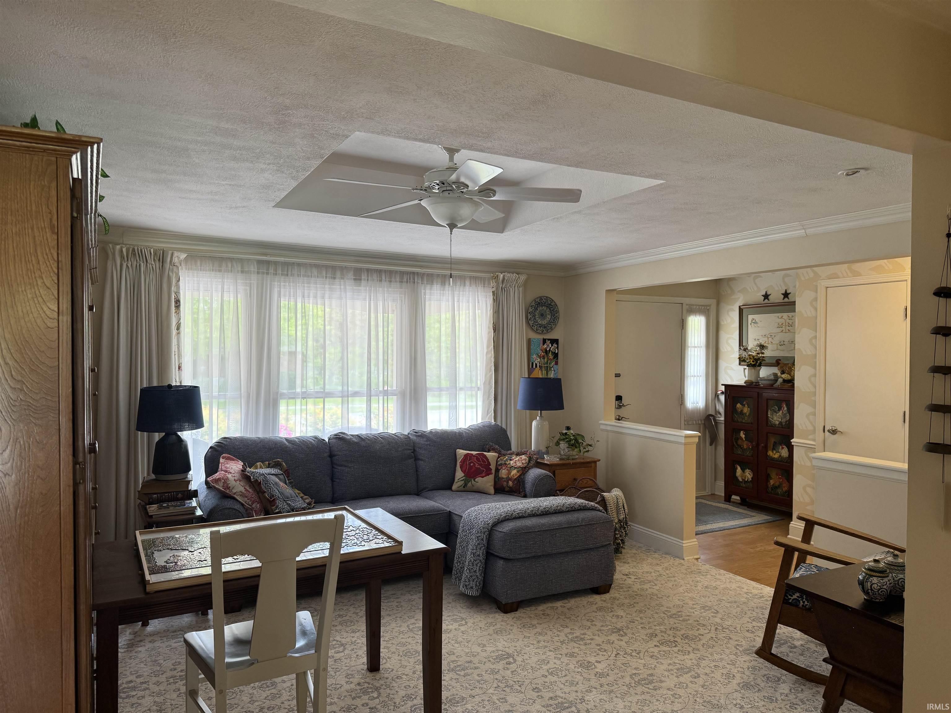 Spacious living area featuring a large window, ceiling fan, crown molding, and wood-finish flooring in the entryway