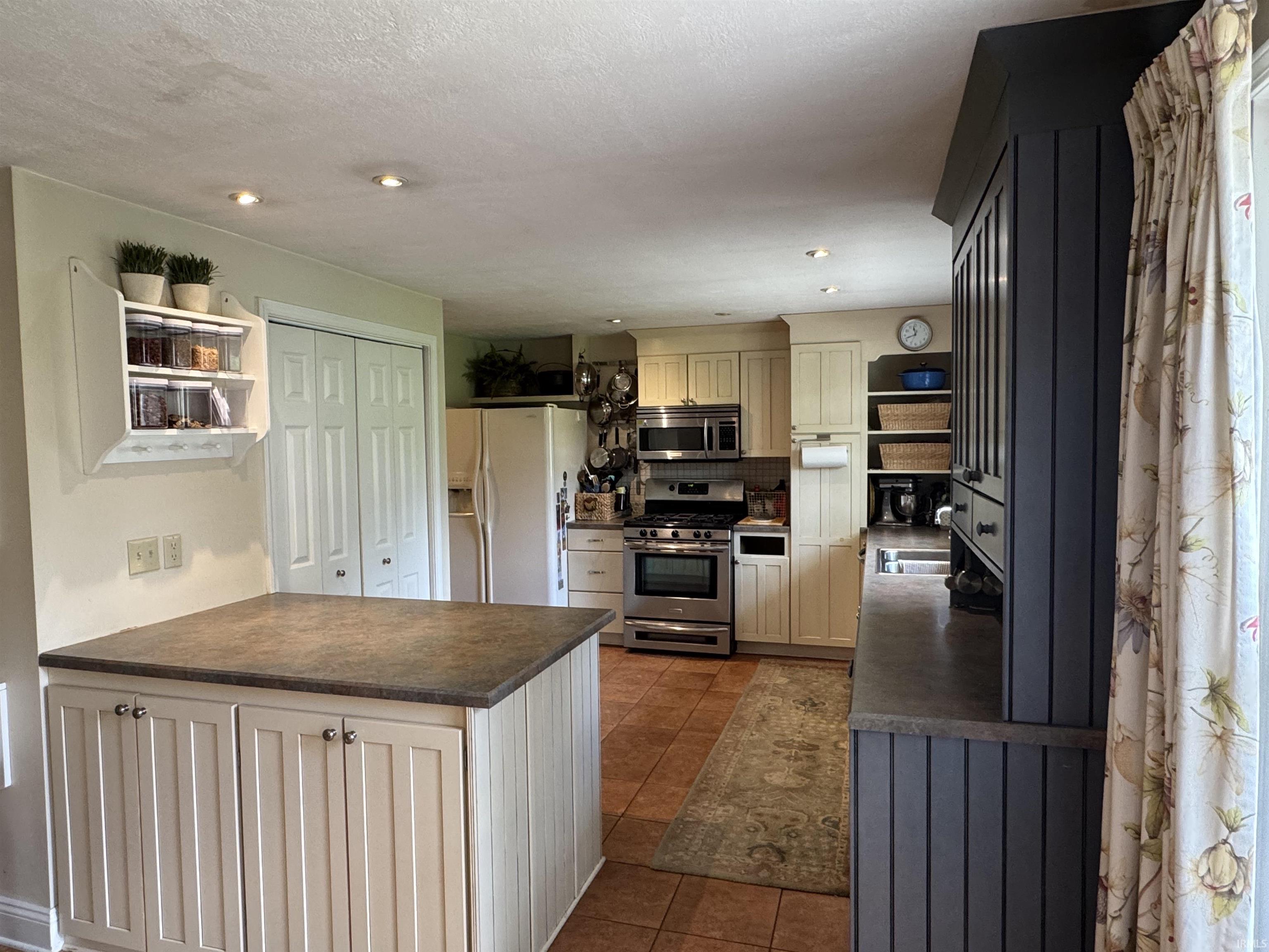Kitchen featuring a central island with a solid surface countertop, stainless steel appliances, recessed lighting, tile flooring, and a built-in pantry with bi-fold doors