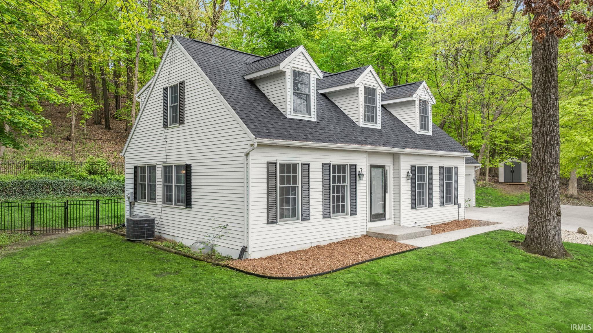 White siding exterior featuring black shutters, a dark shingle roof, and three dormer windows