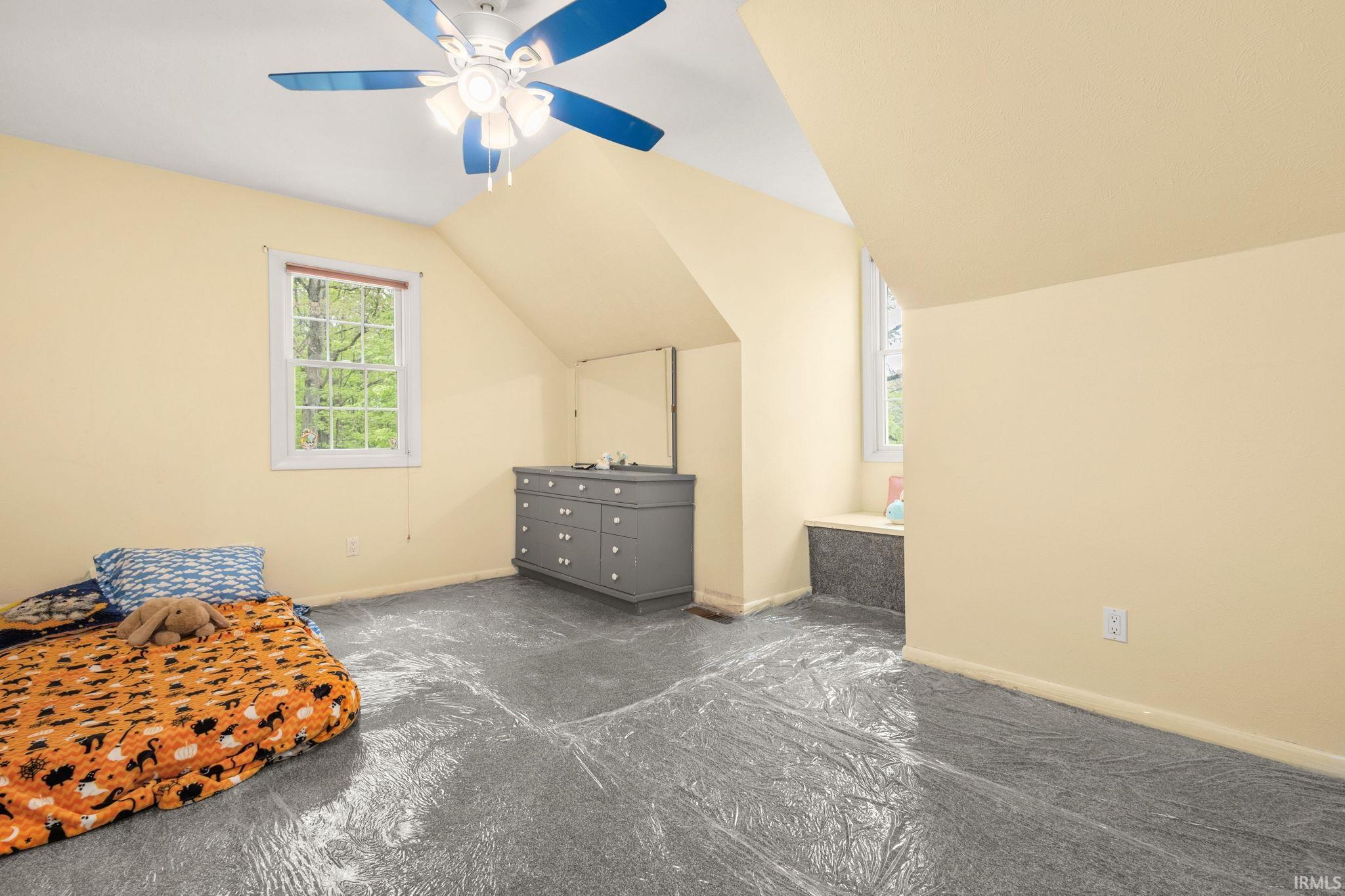 Room featuring an angled ceiling, a ceiling fan with light fixture, and a window with white trim