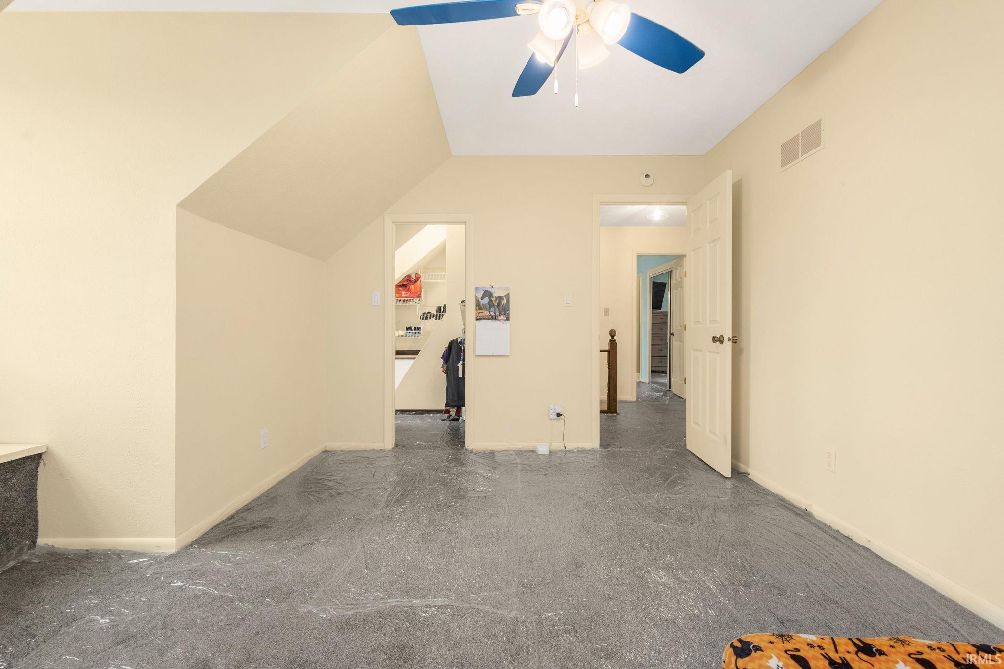 Attic space featuring sloped ceilings, ceiling fan, and access to additional rooms