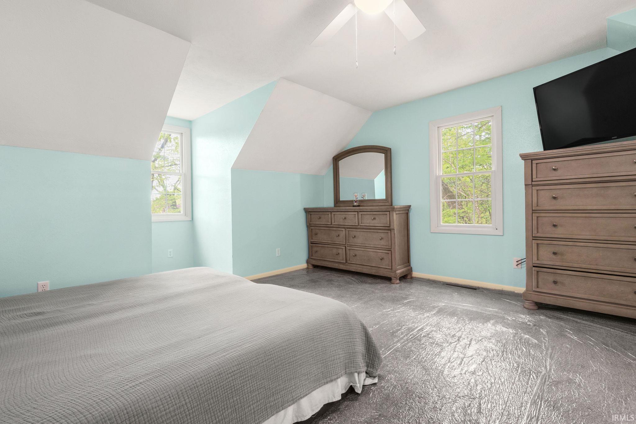 Attic space featuring pitched ceilings, two windows, and a ceiling fan