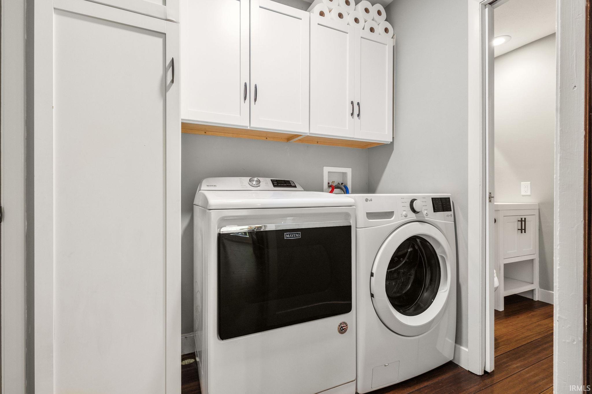 Laundry area featuring white cabinetry, a wood shelf, and dark wood-finish flooring
