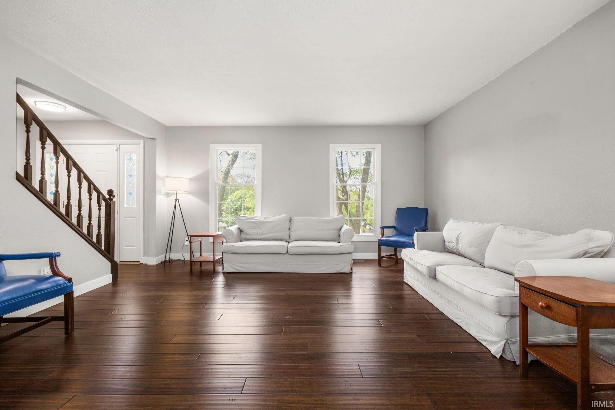 Spacious living area featuring rich wood-finish flooring, light grey wall paint, and multiple windows