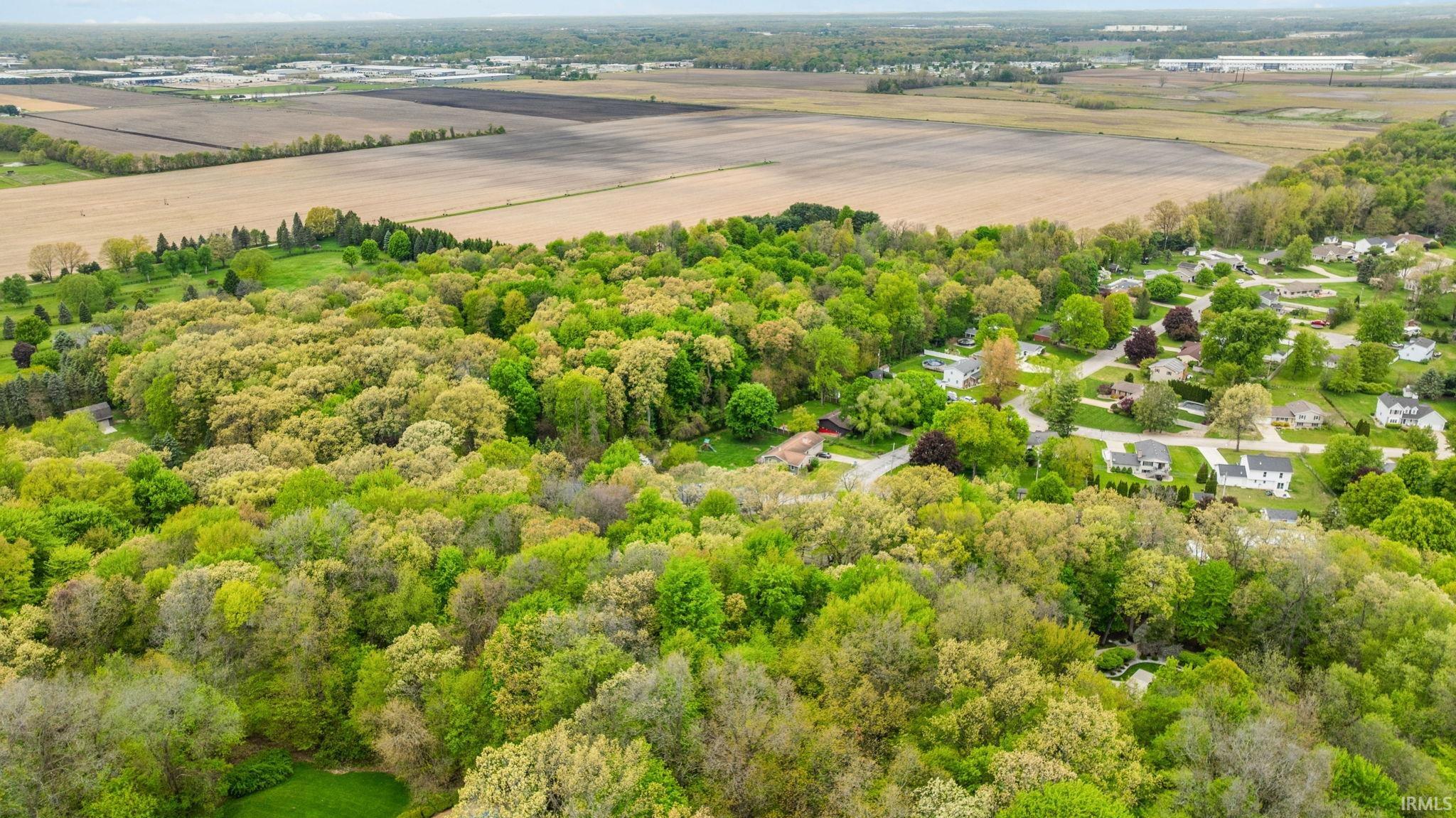 Expansive aerial perspective showcasing a residential area enveloped by mature trees, bordering agricultural fields