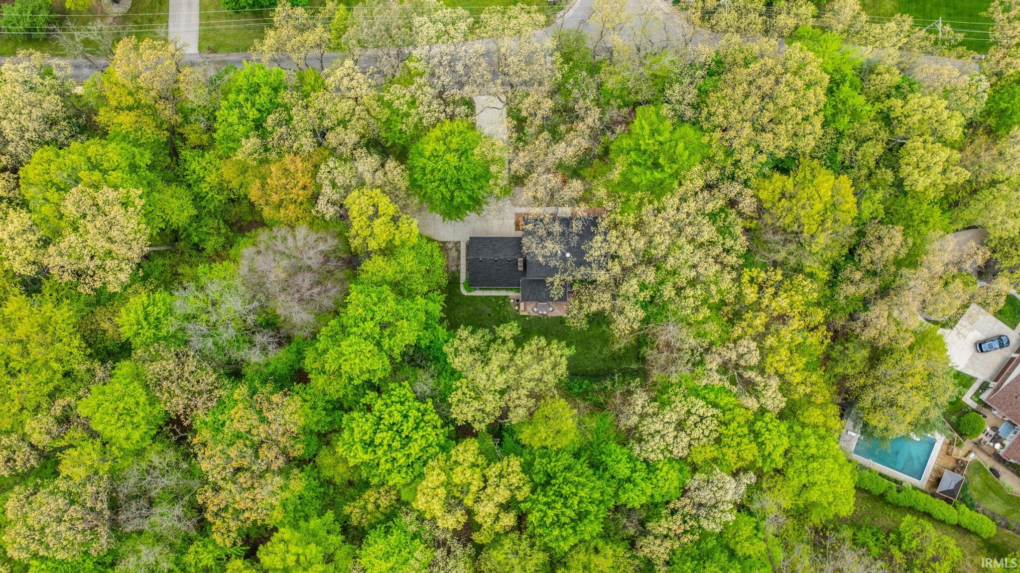 Wooded property featuring a single-family residence with a dark shingle roof and brick exterior accents