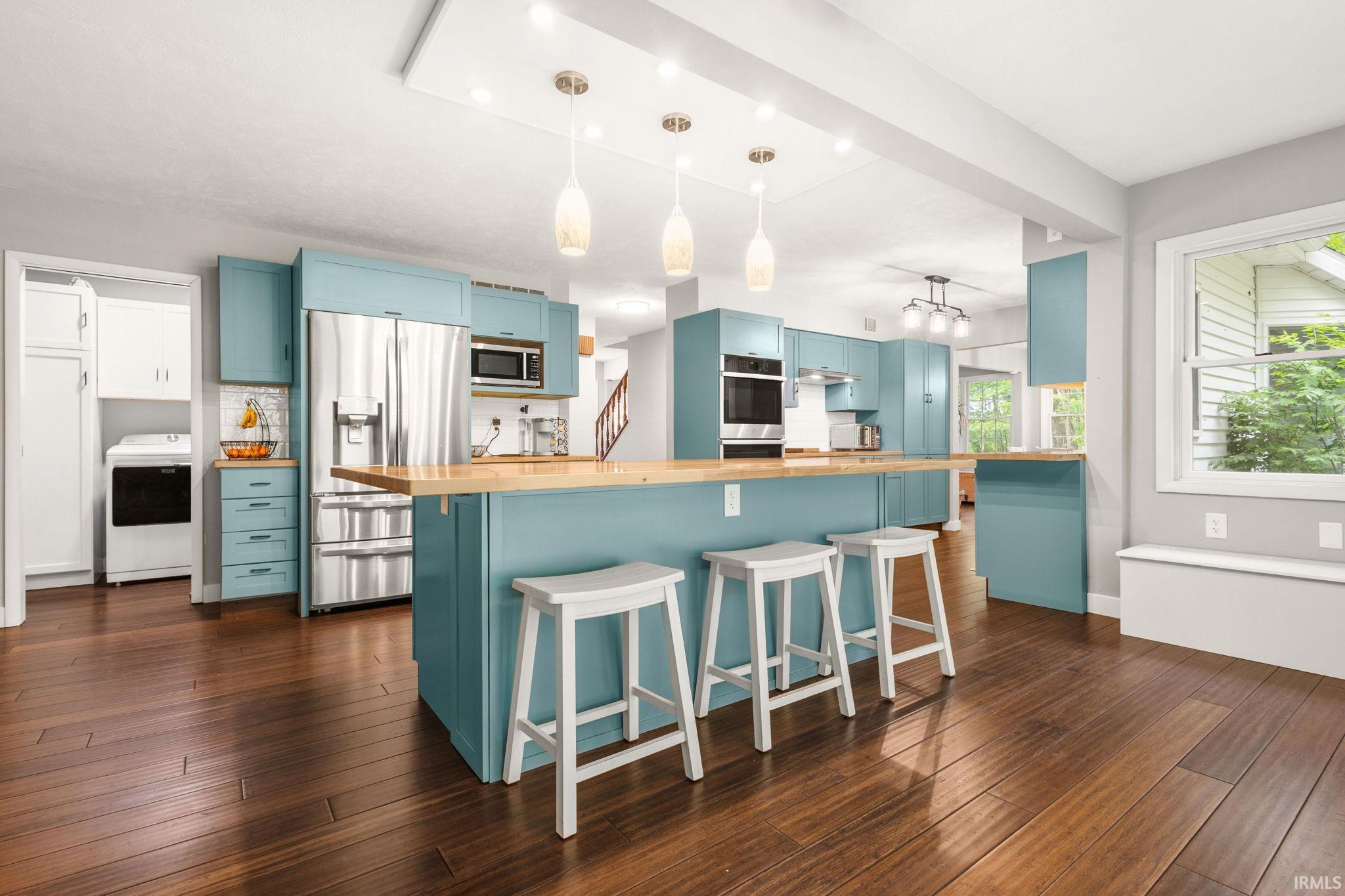 Spacious kitchen featuring a large central island with seating, wood-finish countertops, stainless steel appliances, and abundant cabinetry