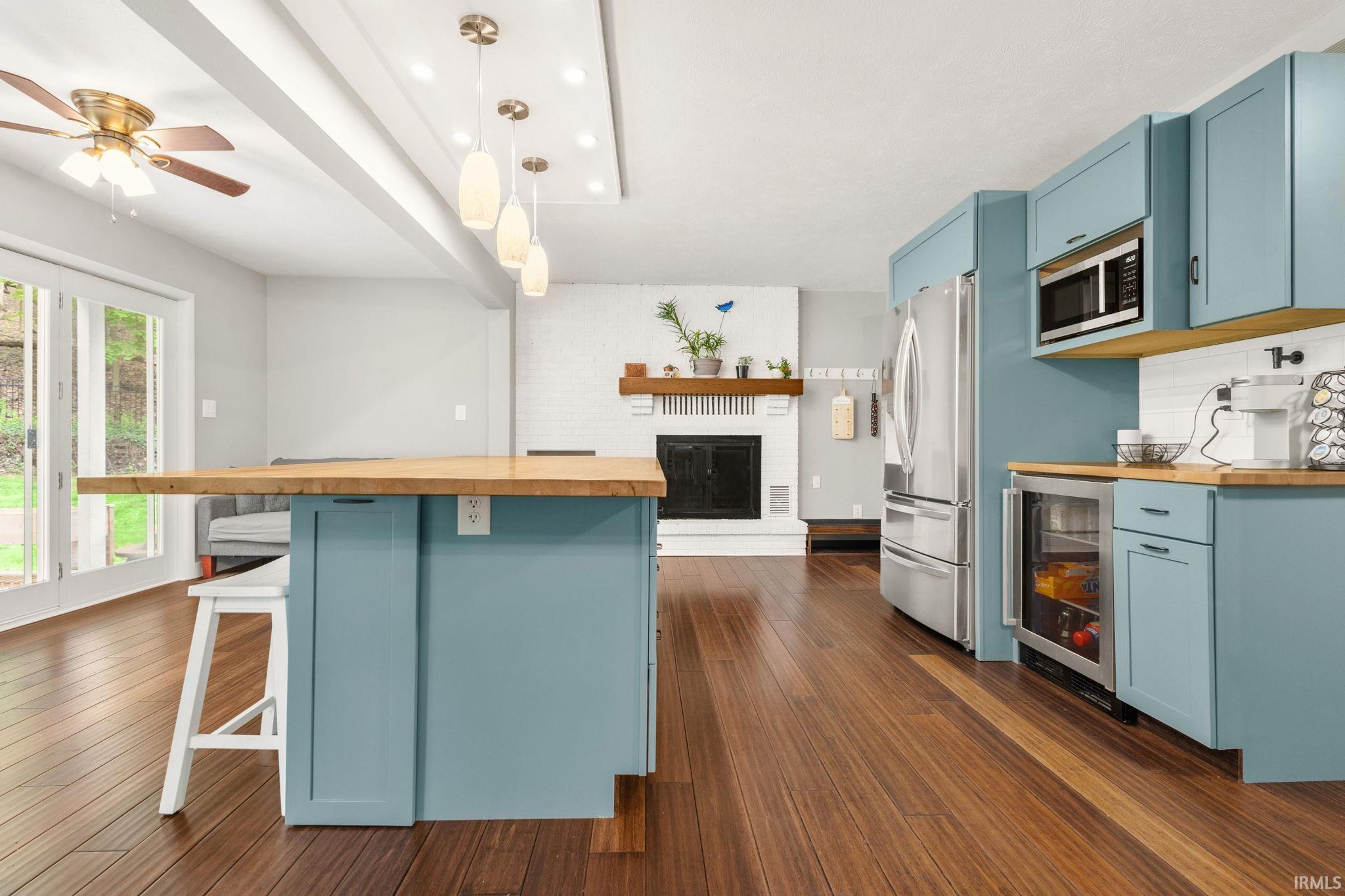 Open-concept living area featuring a kitchen island with wood countertop, light blue cabinetry, stainless steel appliances, and wood-finish flooring