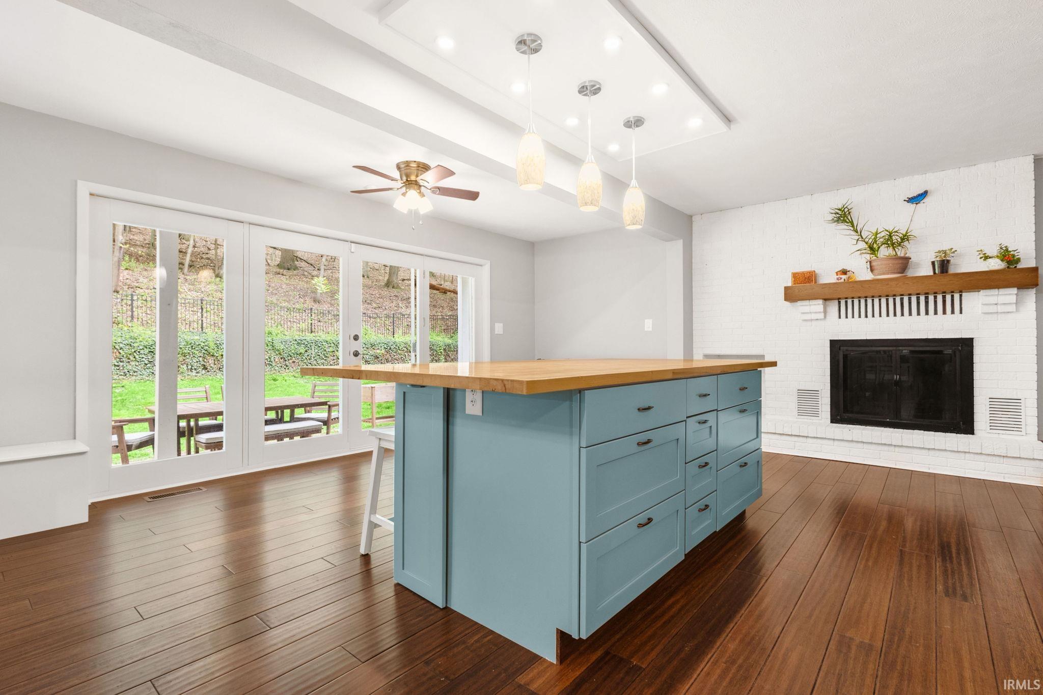 Spacious room featuring wood-finish flooring, a contemporary blue island with a wood countertop, and a white brick fireplace with a wood mantel