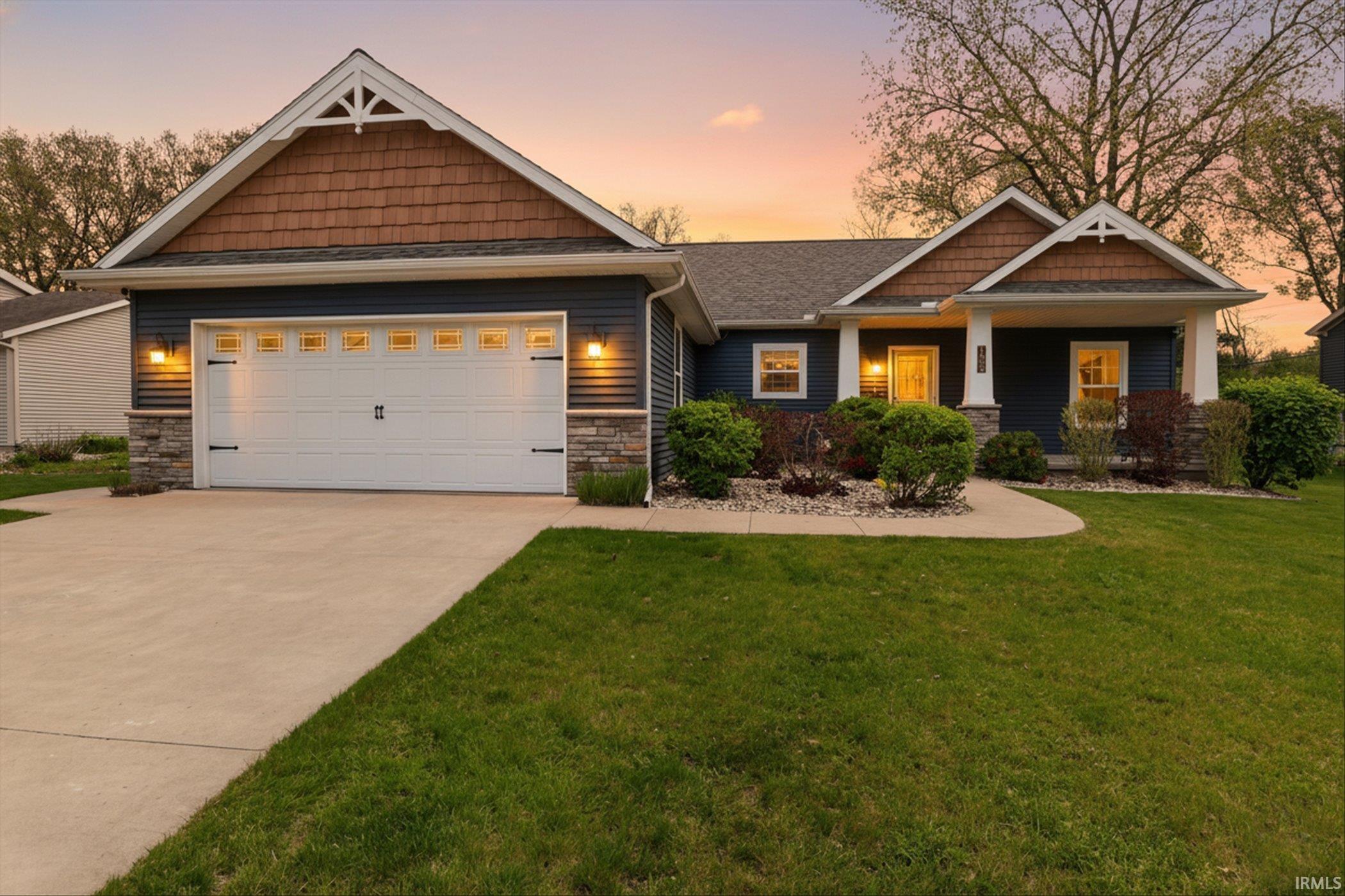 Craftsman-style home featuring a two-car garage, dark blue siding, stone facade accents, cedar shake gables, and a covered porch with white columns