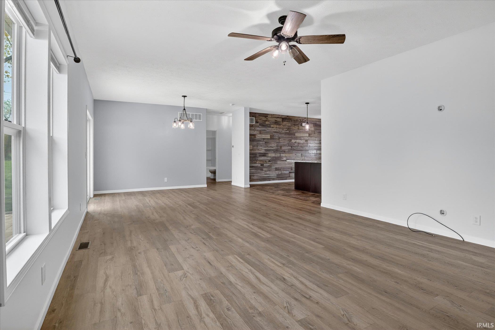 Spacious interior with wood-finish flooring, ample natural light from multiple windows, and a ceiling fan