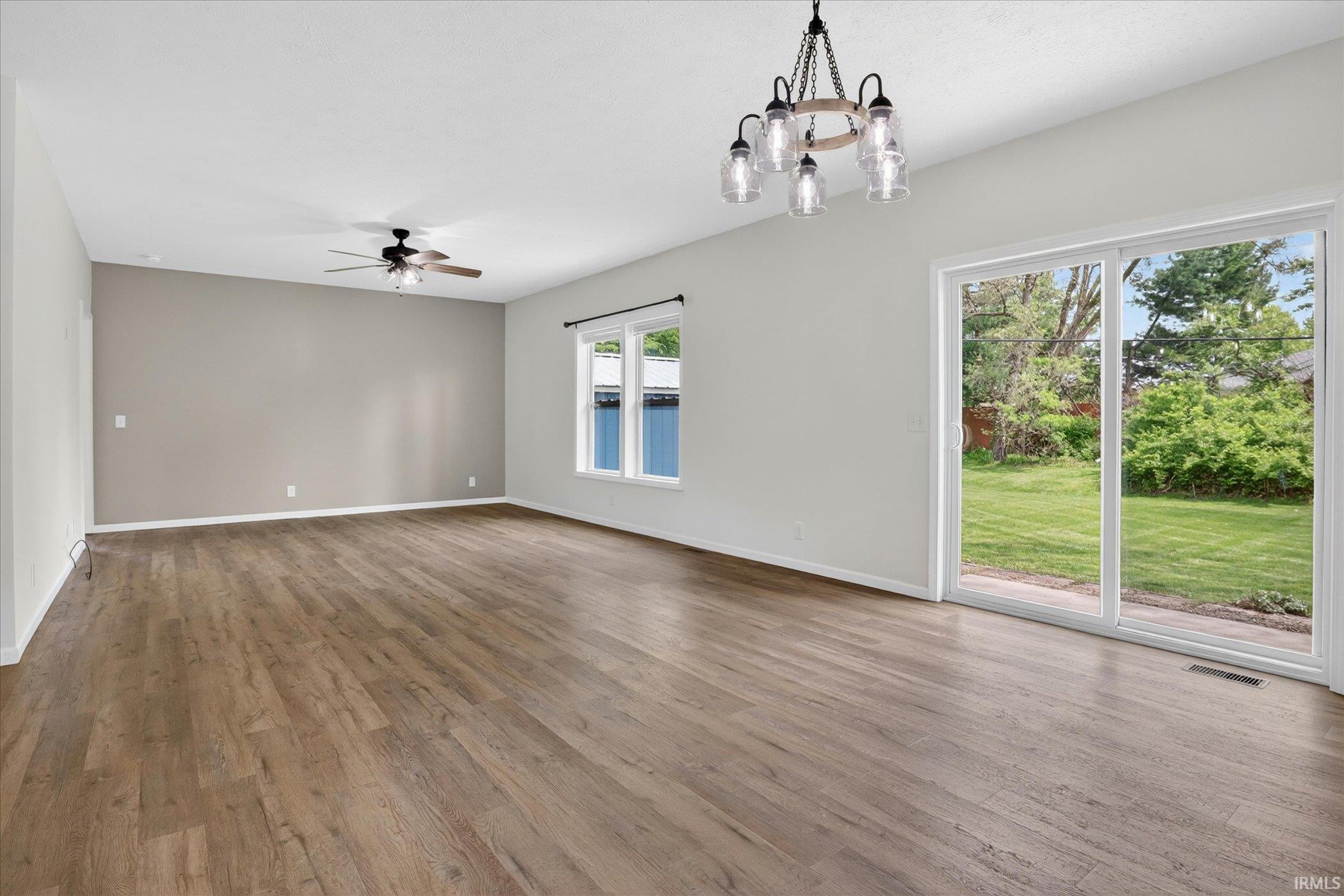 Spacious interior featuring wood-finish flooring, a contemporary ceiling fan, and a rustic-inspired chandelier
