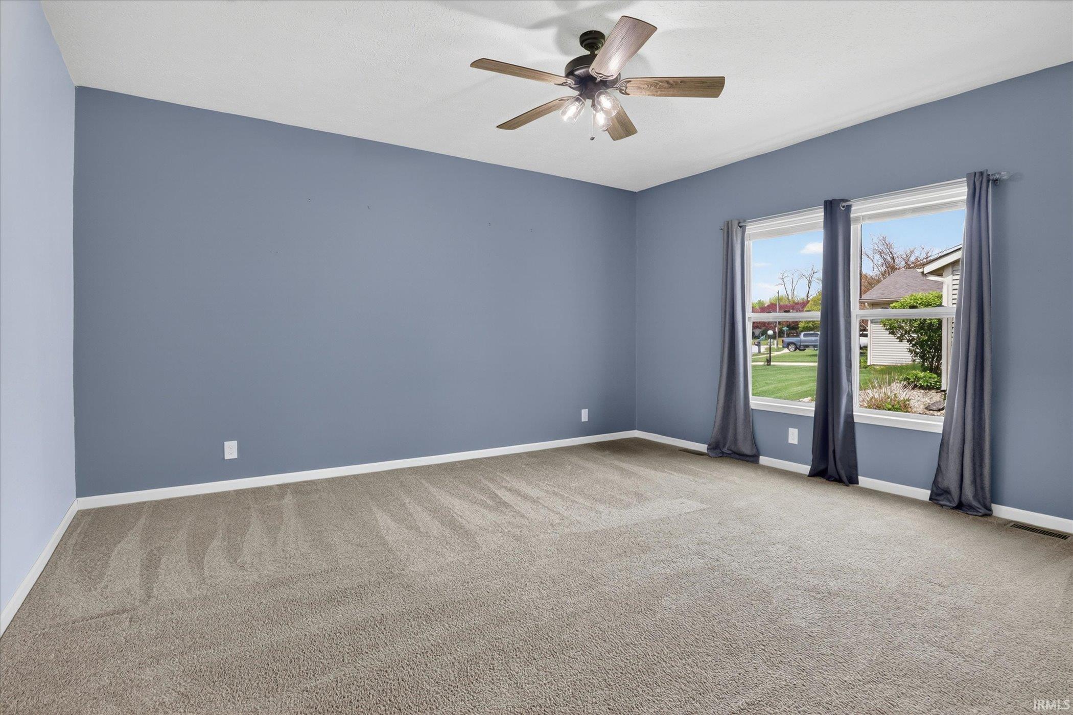 Spacious room featuring light blue walls and neutral-toned carpeting