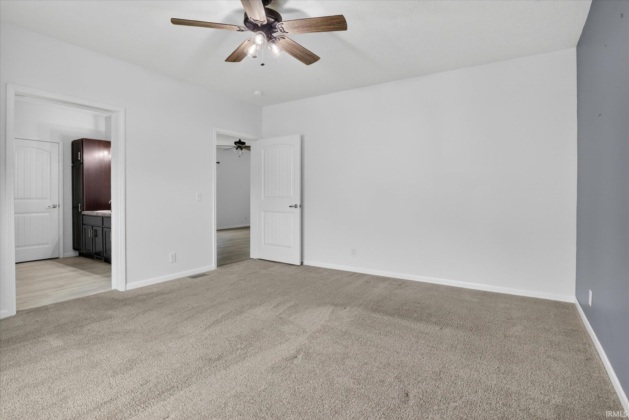 Spacious room featuring neutral carpet flooring, white walls, and a ceiling fan with wood-finish blades