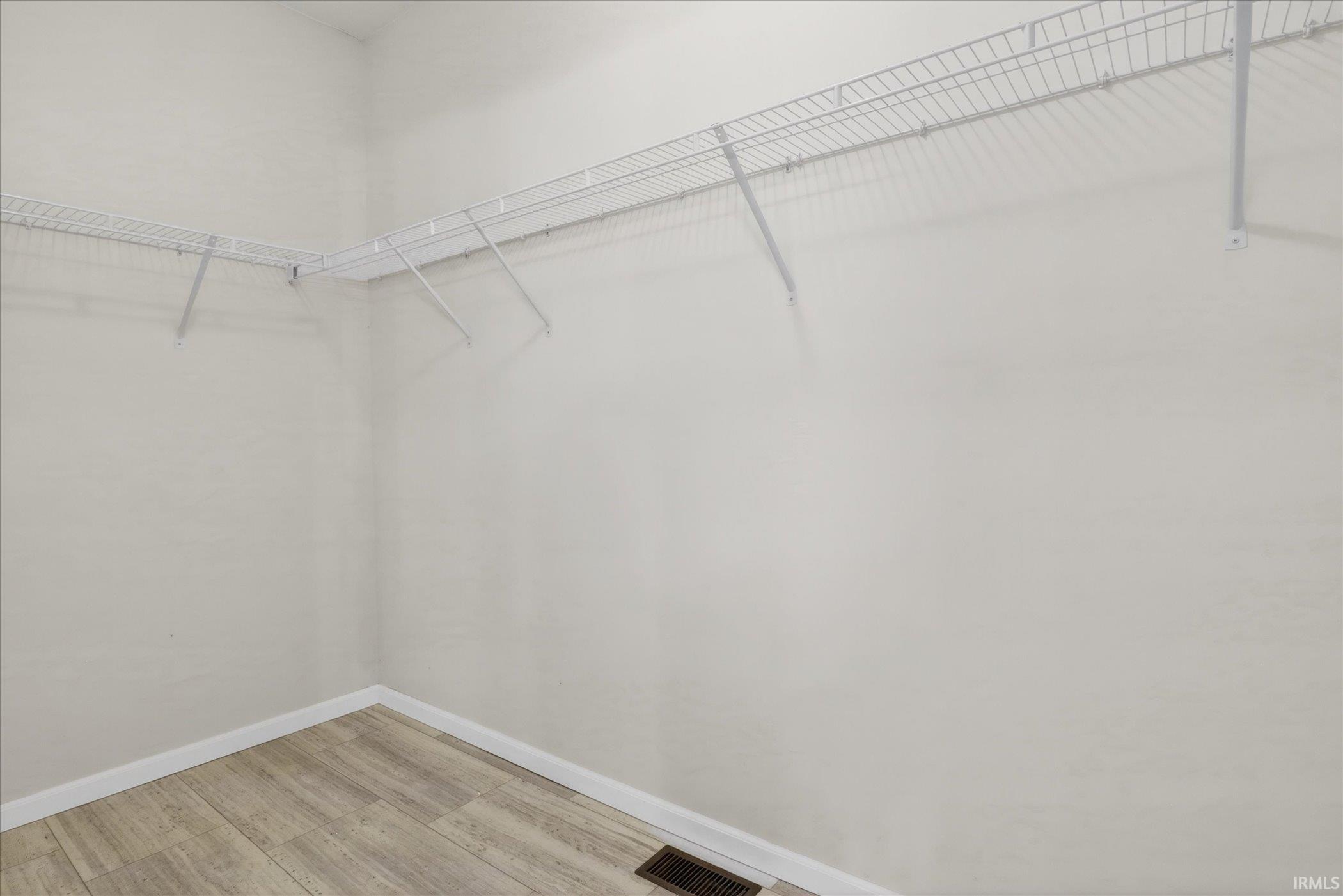 Interior closet featuring wire shelving, light-toned wood-finish flooring, and white baseboards
