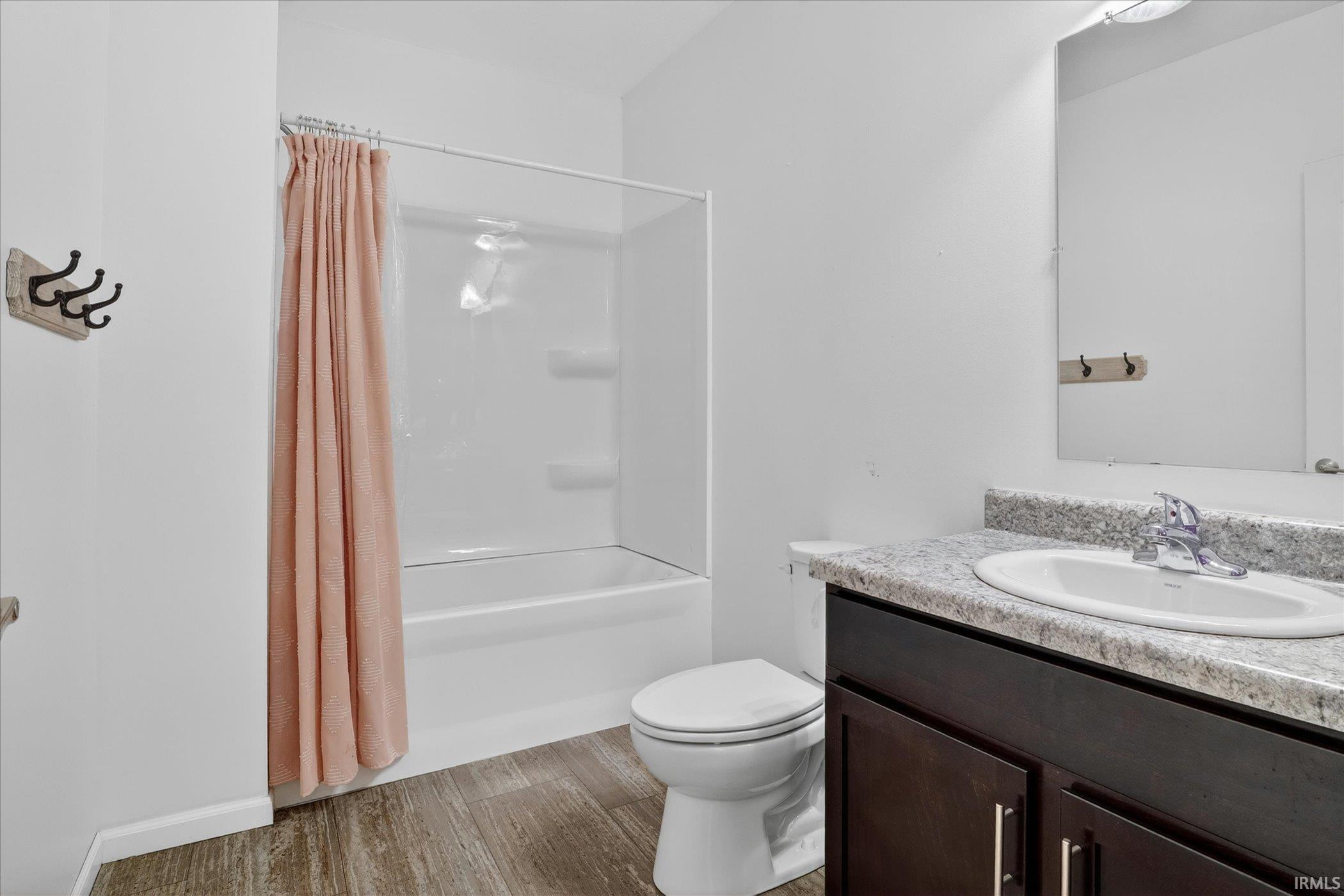 Bathroom featuring a shower-tub combination, wood-finish flooring, a dark wood-finish vanity with a light-colored countertop, and a wall-mounted mirror