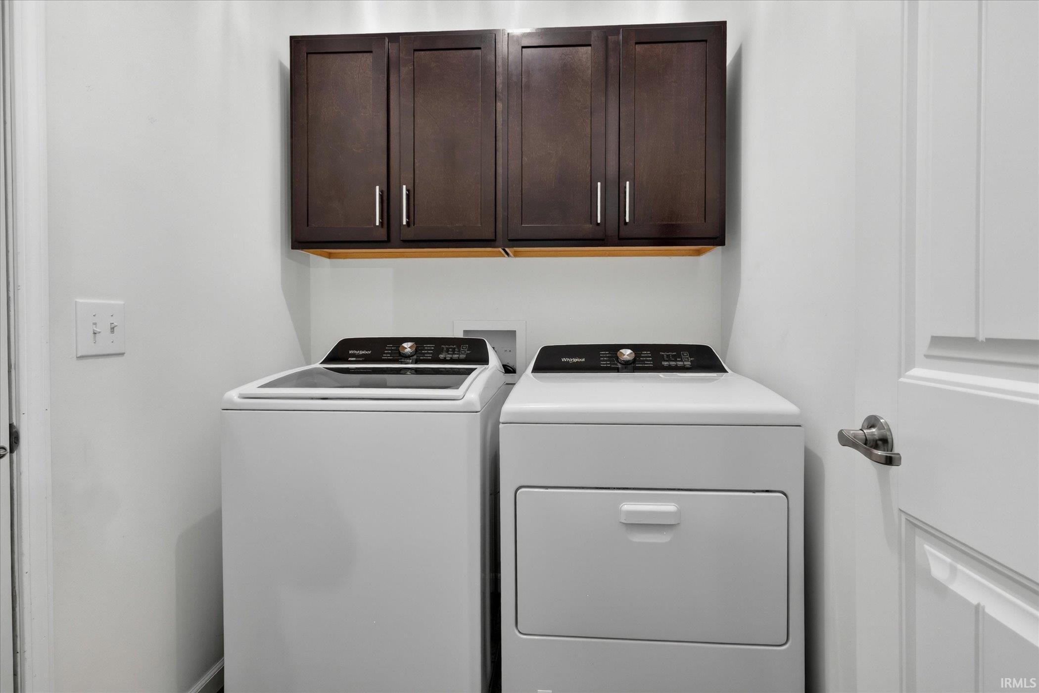 Dedicated laundry area featuring dark wood-finish cabinetry, a light wood-finish shelf, and white walls