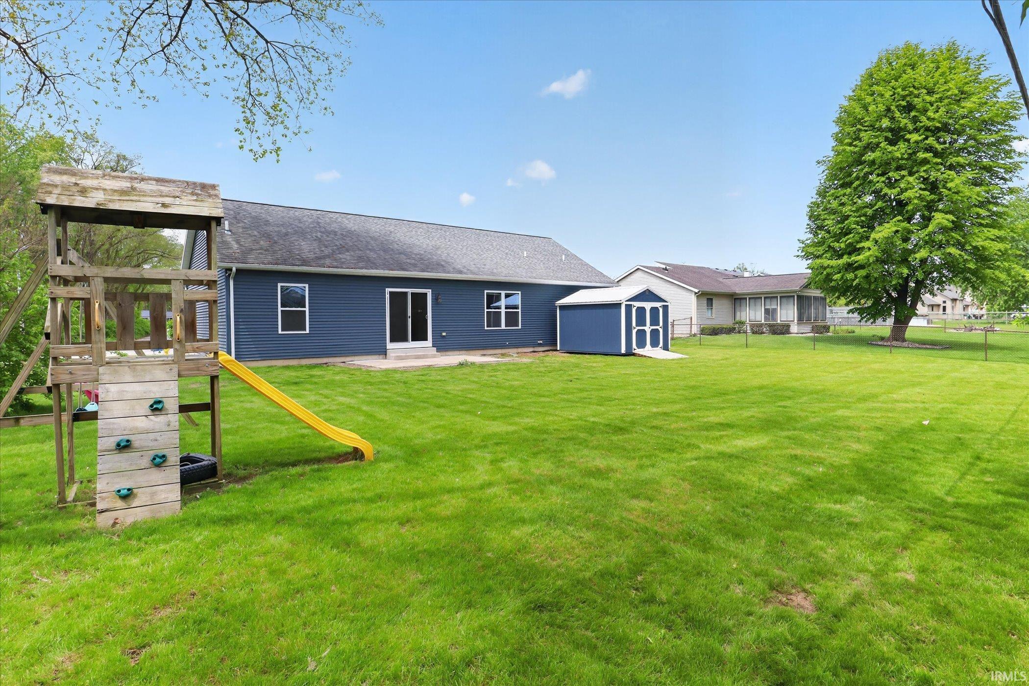 Spacious backyard featuring a large green lawn, a blue siding storage shed, and a mature tree