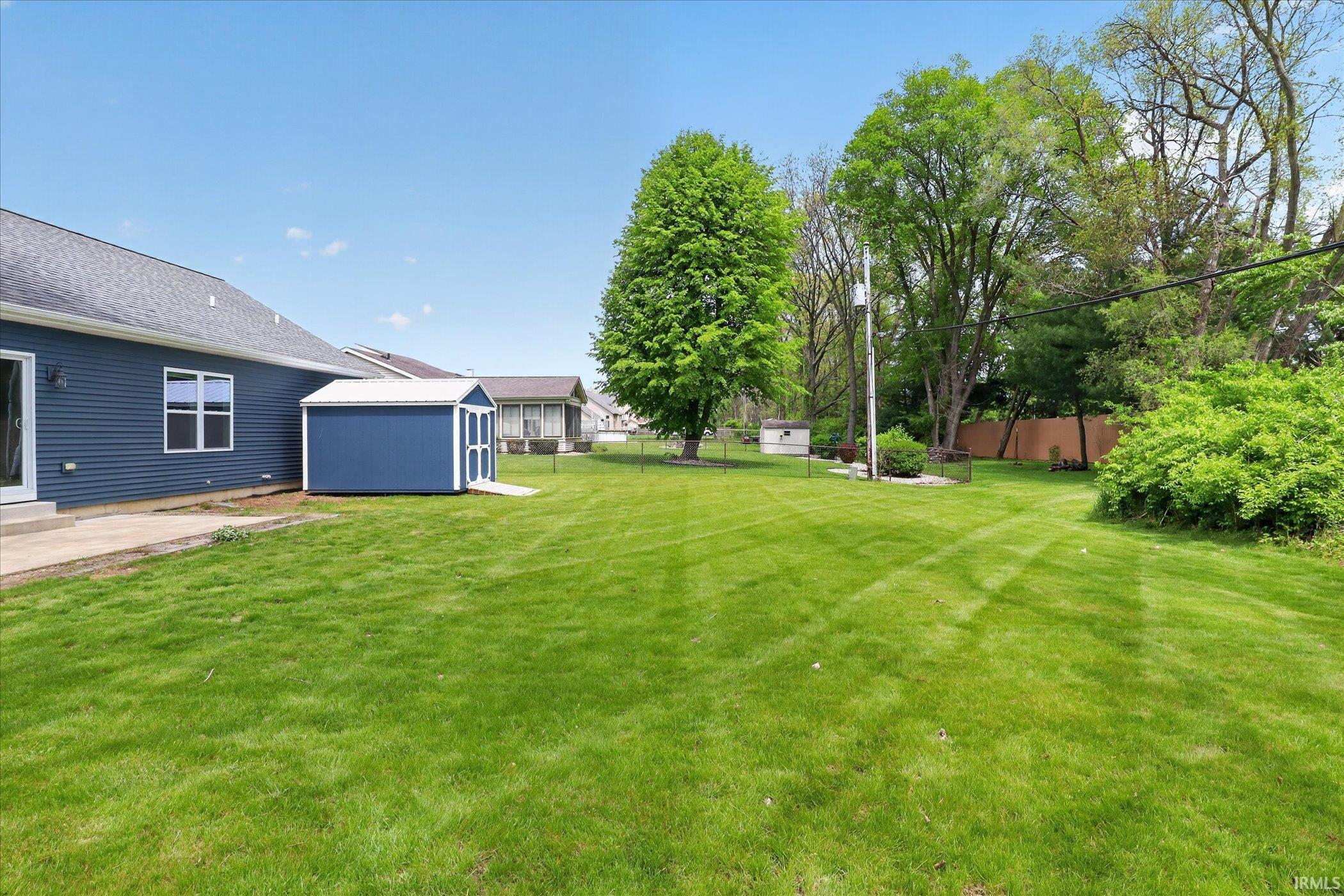 Expansive rear yard featuring a large blue shed with white trim, mature trees, and a concrete patio