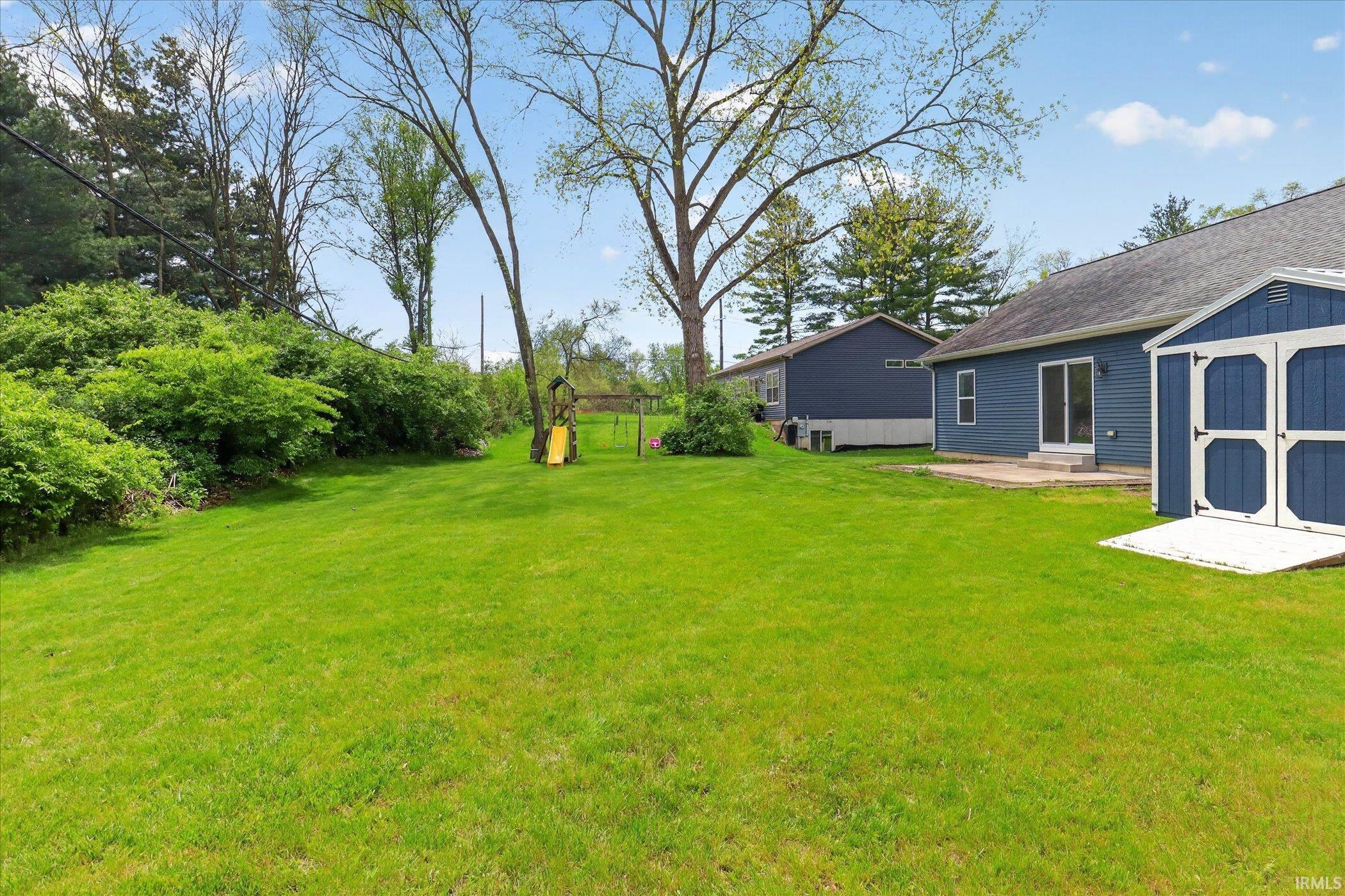 Spacious rear lawn with vibrant green grass, mature trees, and dense perimeter shrubbery