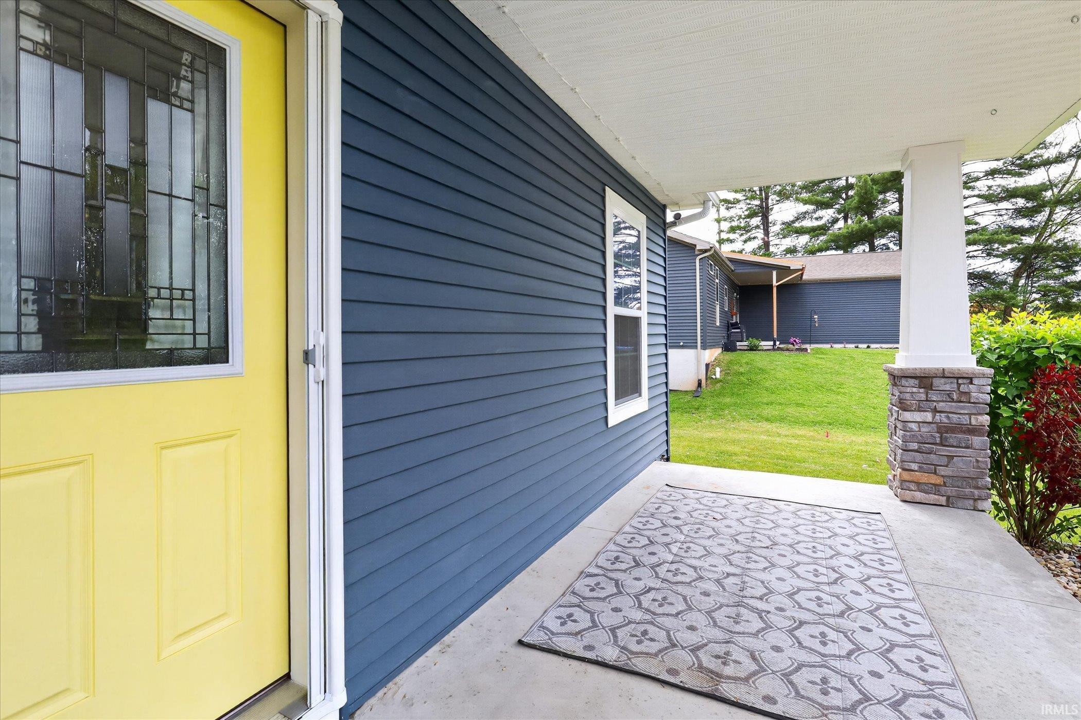 Inviting front porch featuring a vibrant yellow door with decorative glass, blue horizontal siding, and a stone-clad column