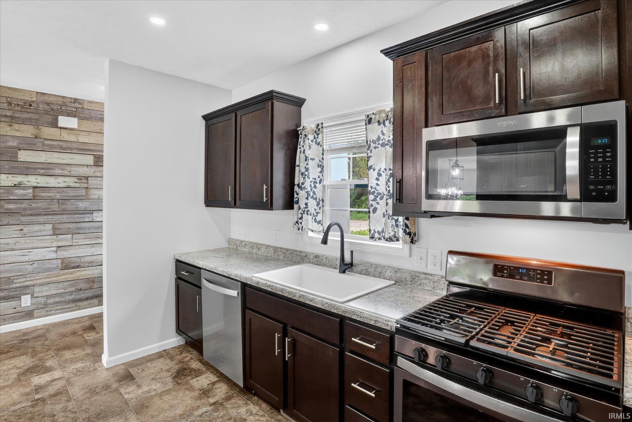 Kitchen featuring dark wood cabinetry, light-toned granite-style countertops, stainless steel appliances, and a white subway tile backsplash
