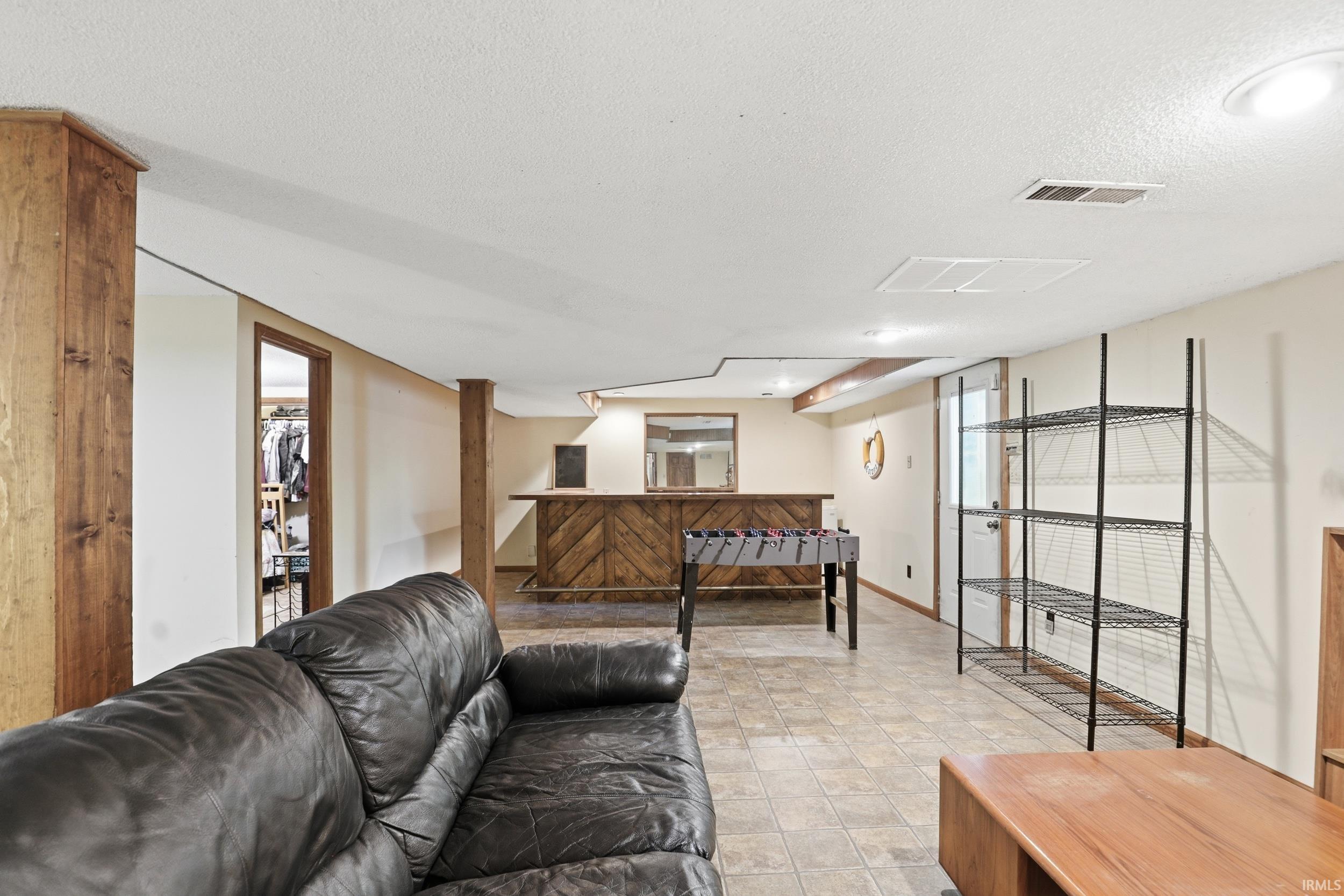 Finished lower level featuring a built-in bar with wood-paneled detailing, recessed lighting, and tile flooring