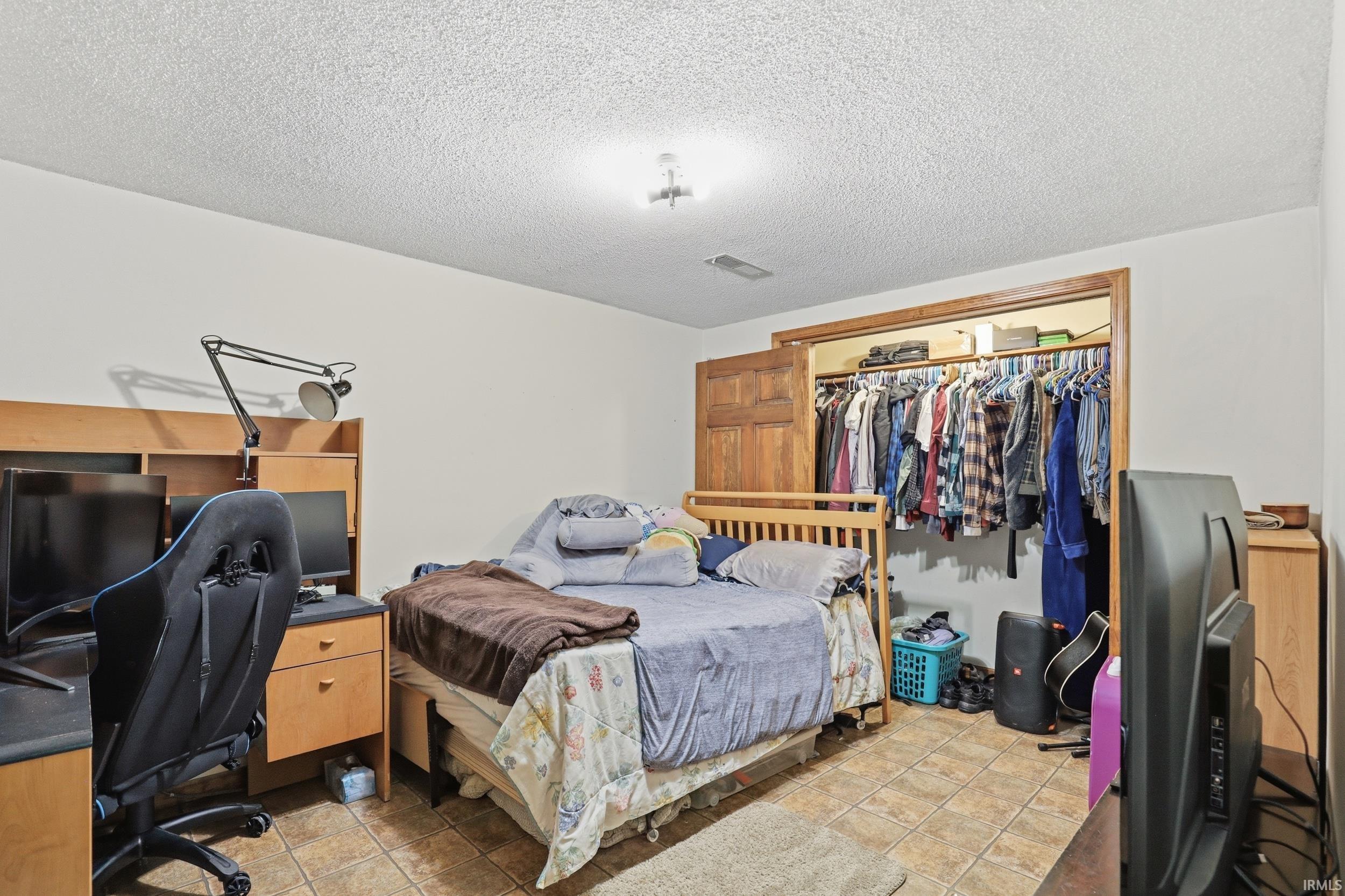 Room featuring tile flooring, a built-in closet with wooden bi-fold doors, and a wood-finish bed frame