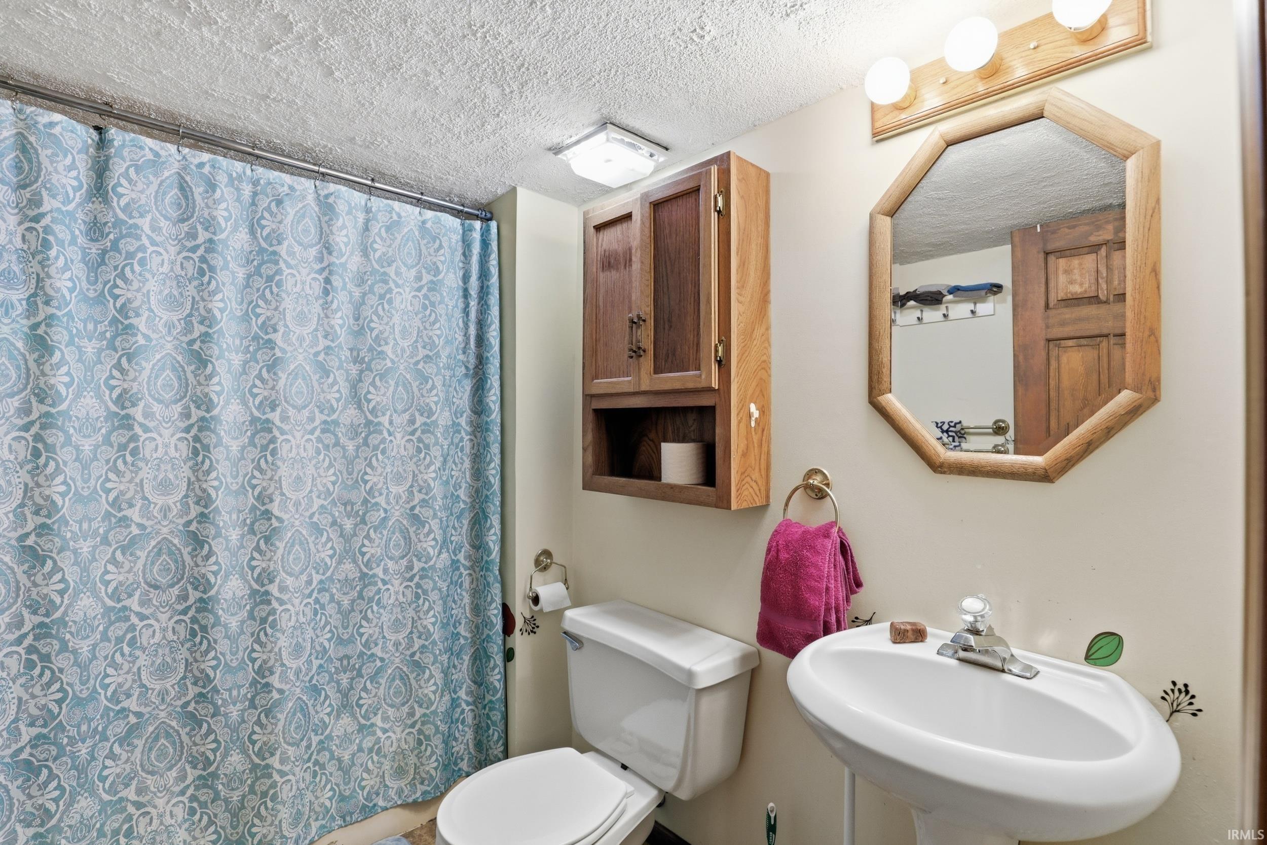 Bathroom featuring a white pedestal sink, toilet, and a medicine cabinet with open shelving
