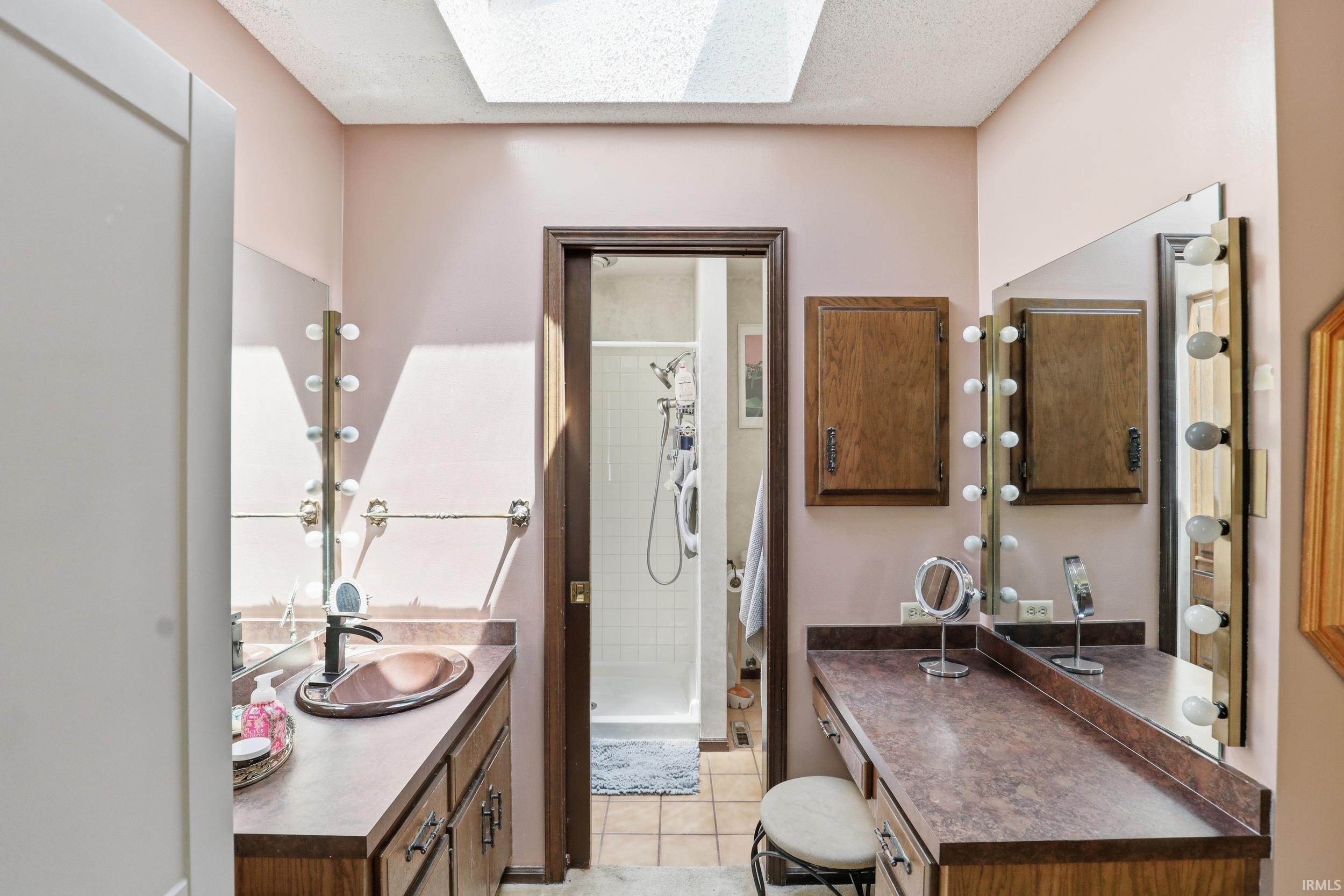 Bathroom featuring a skylight, a vanity with an integrated sink, a separate makeup vanity, built-in cabinetry, and tile flooring