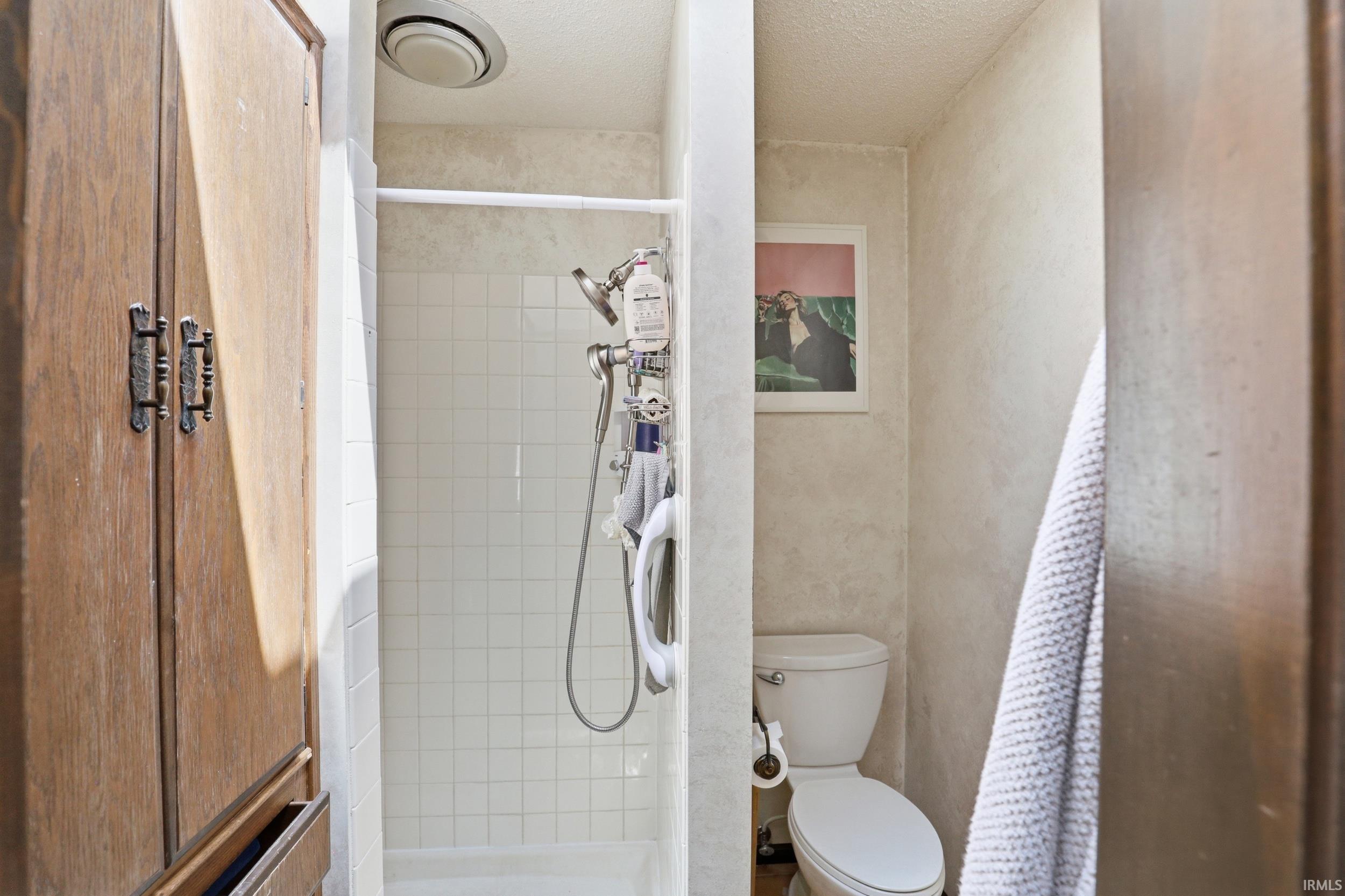 Shower enclosure with white square tile surround, white toilet, and wood-paneled built-in storage
