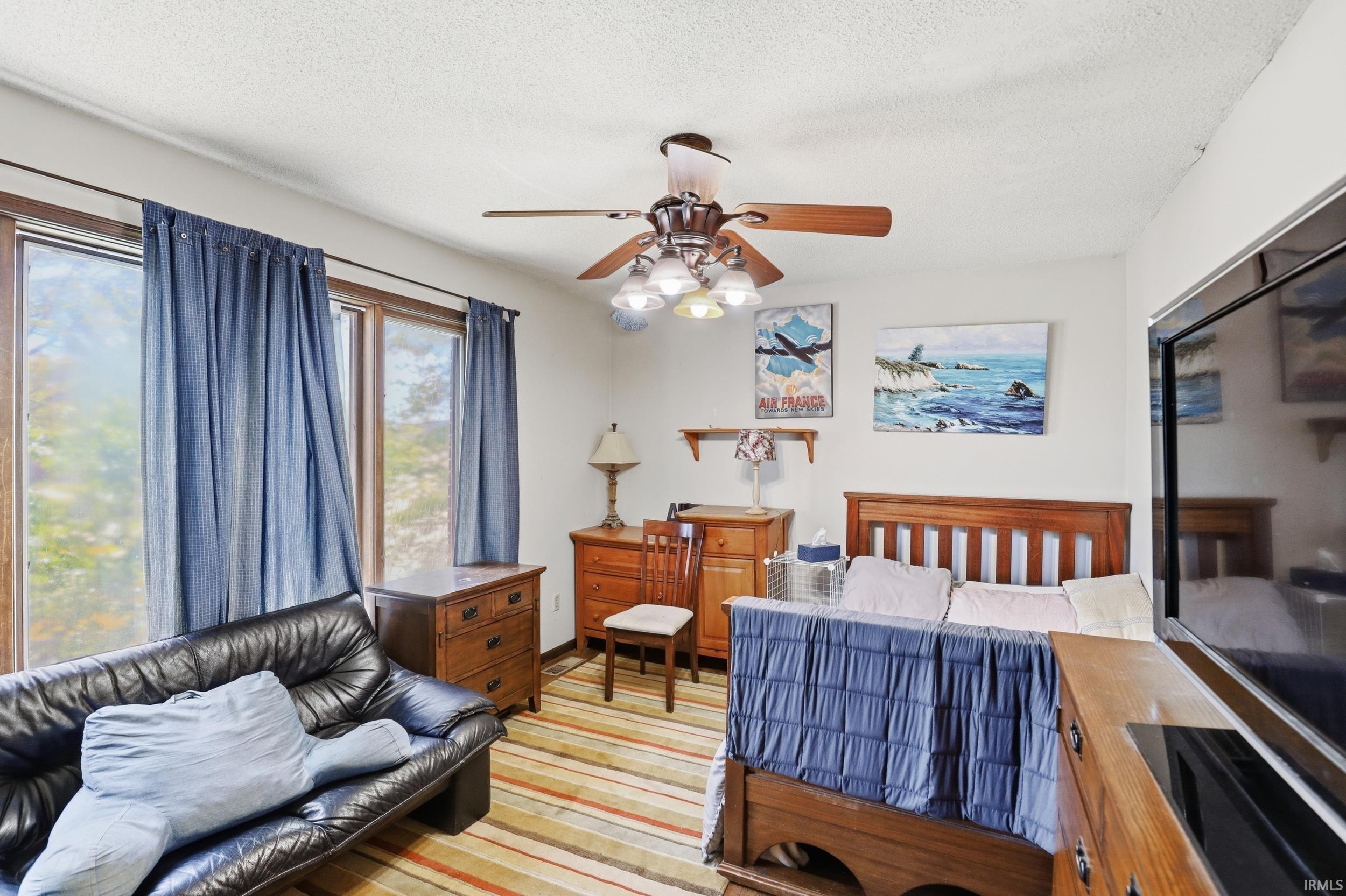 Bedroom featuring a ceiling fan with integrated lighting, wood-finish flooring with a striped area rug, and large windows with natural light