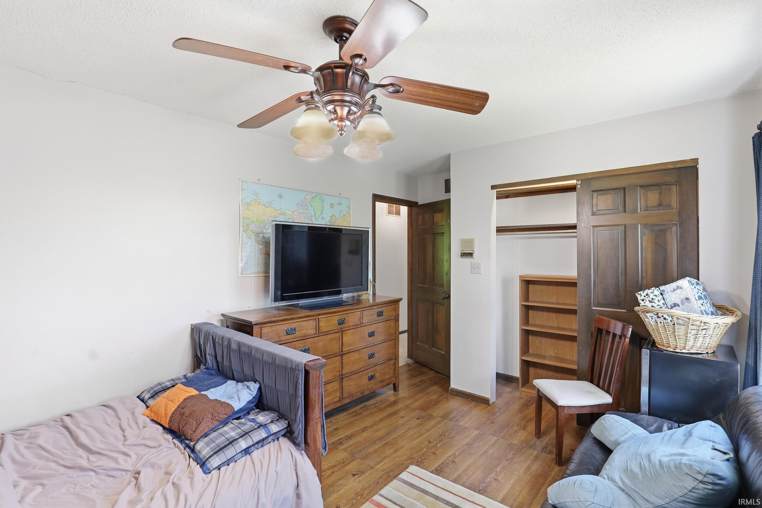 Interior room featuring wood-finish flooring, a ceiling fan with integrated lighting, and a closet with wood-paneled sliding doors