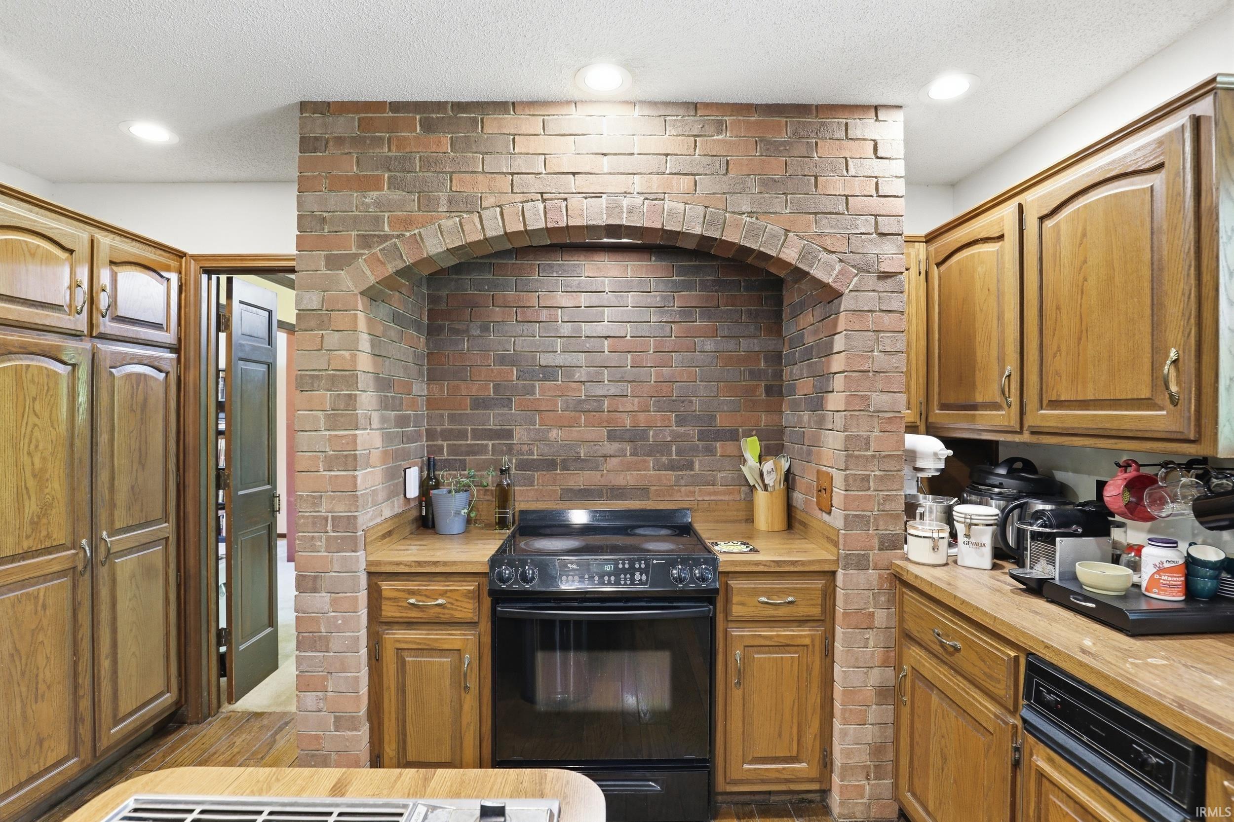 Kitchen featuring an arched brick alcove with a built-in range, wood cabinetry, wood-finish countertops, and recessed lighting