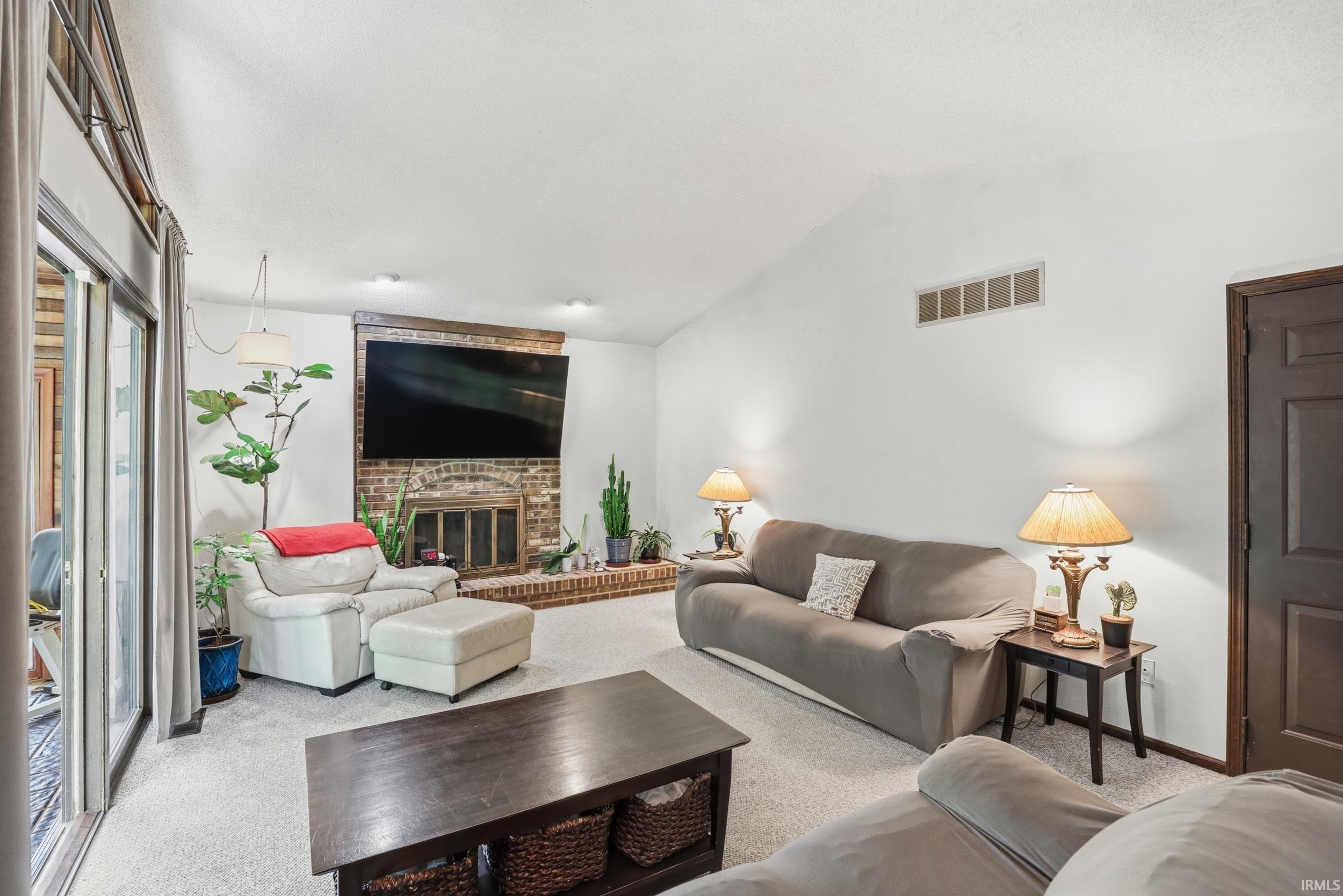 Living area featuring a brick fireplace with a wood mantle, vaulted ceiling, recessed lighting, and a sliding glass door
