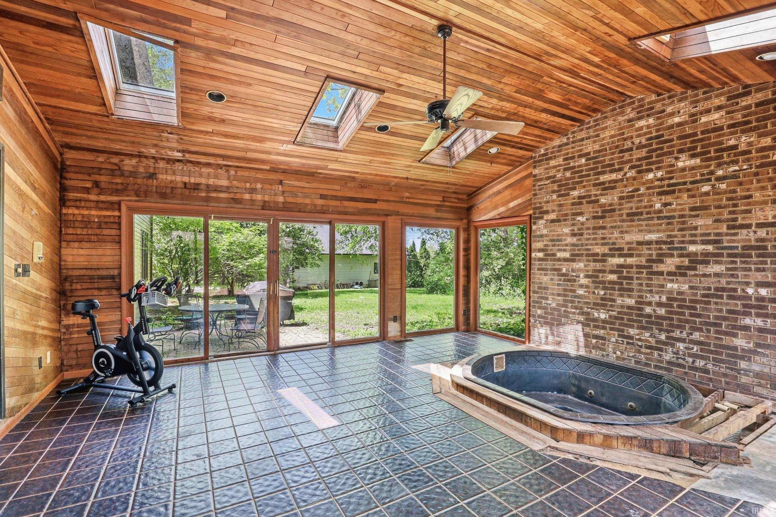 Sunroom featuring wood-paneled walls and ceiling, dark tile flooring, a built-in spa tub, and brick accent wall