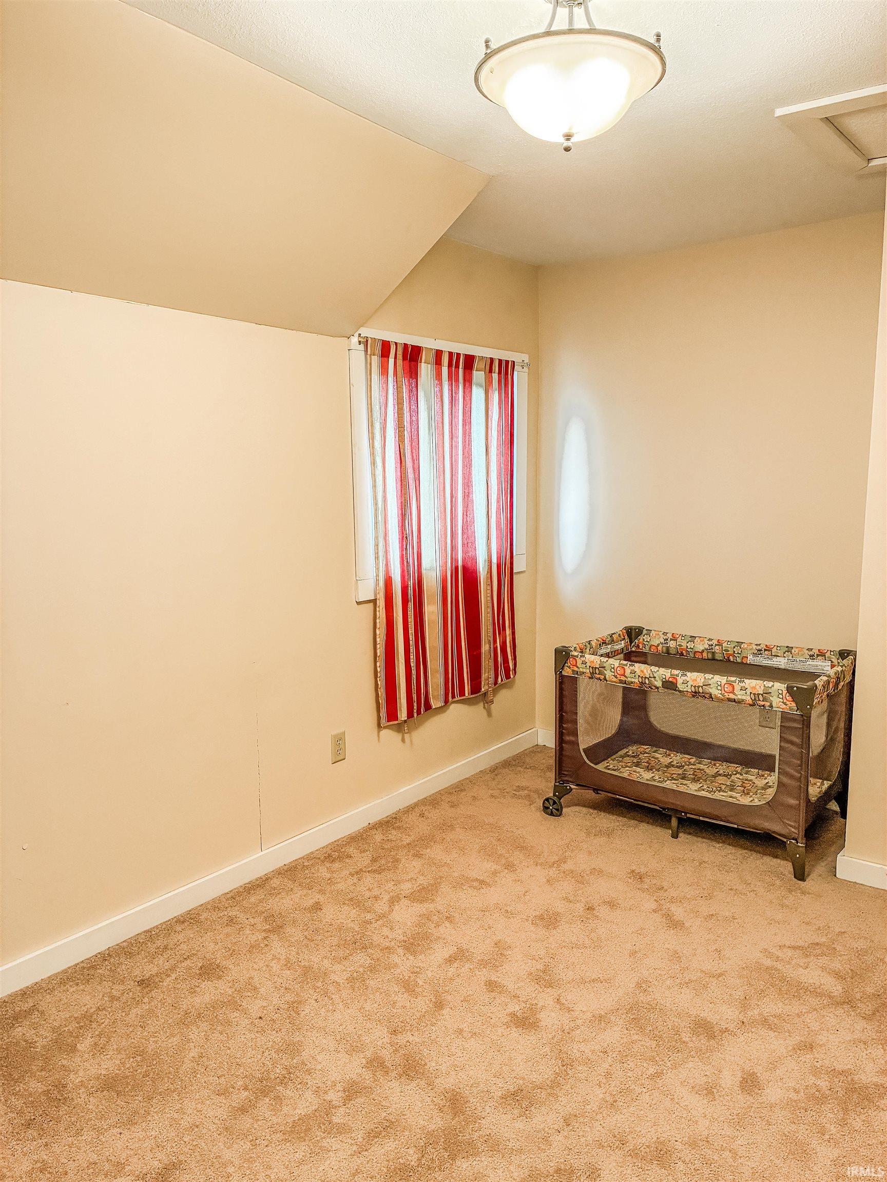 Carpeted room with a ceiling-mounted light fixture, angled wall, and a window with vertical blinds