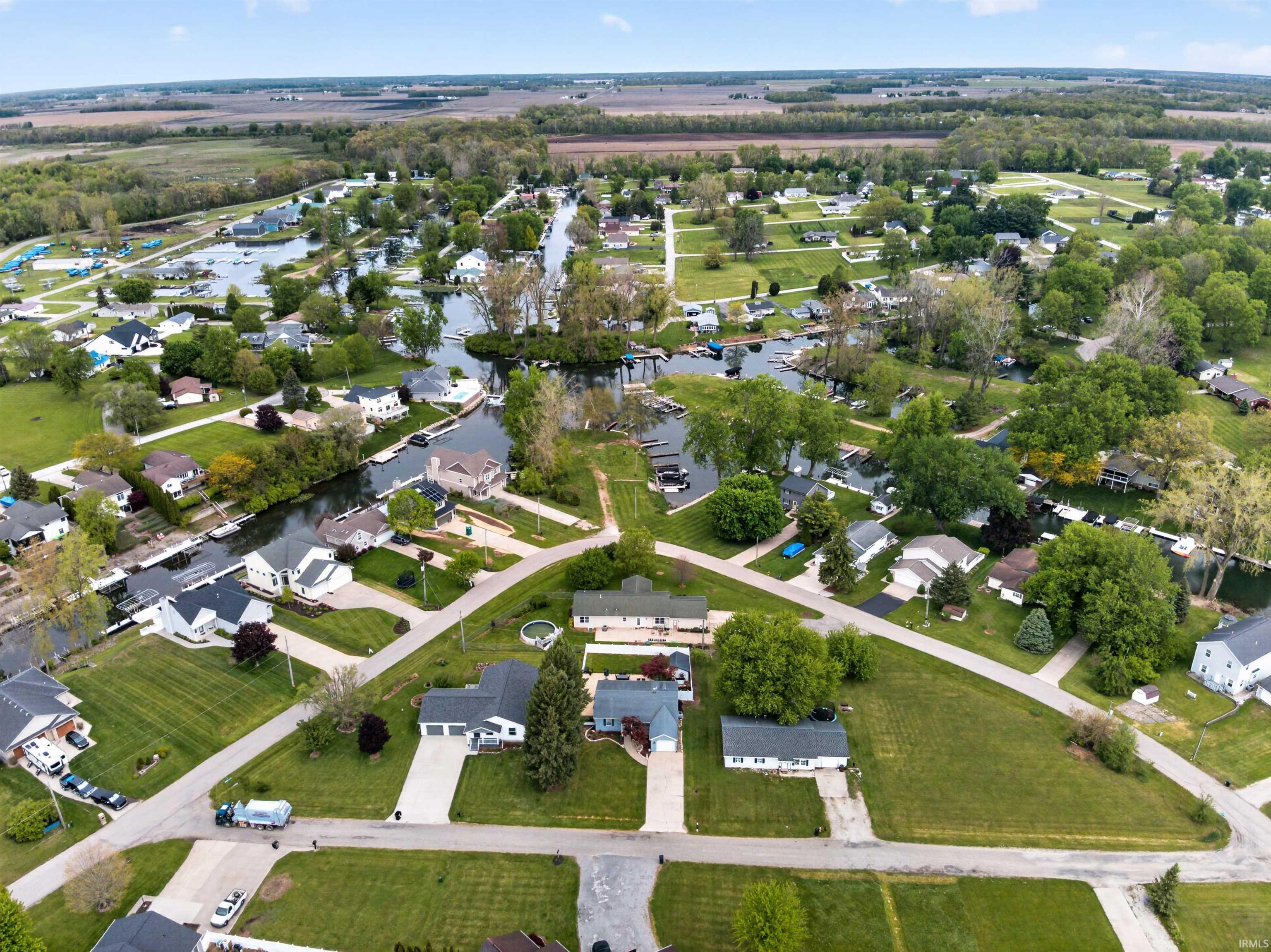 Aerial perspective showcasing a residential area featuring multiple waterways, numerous detached homes, mature trees, and agricultural fields in the background