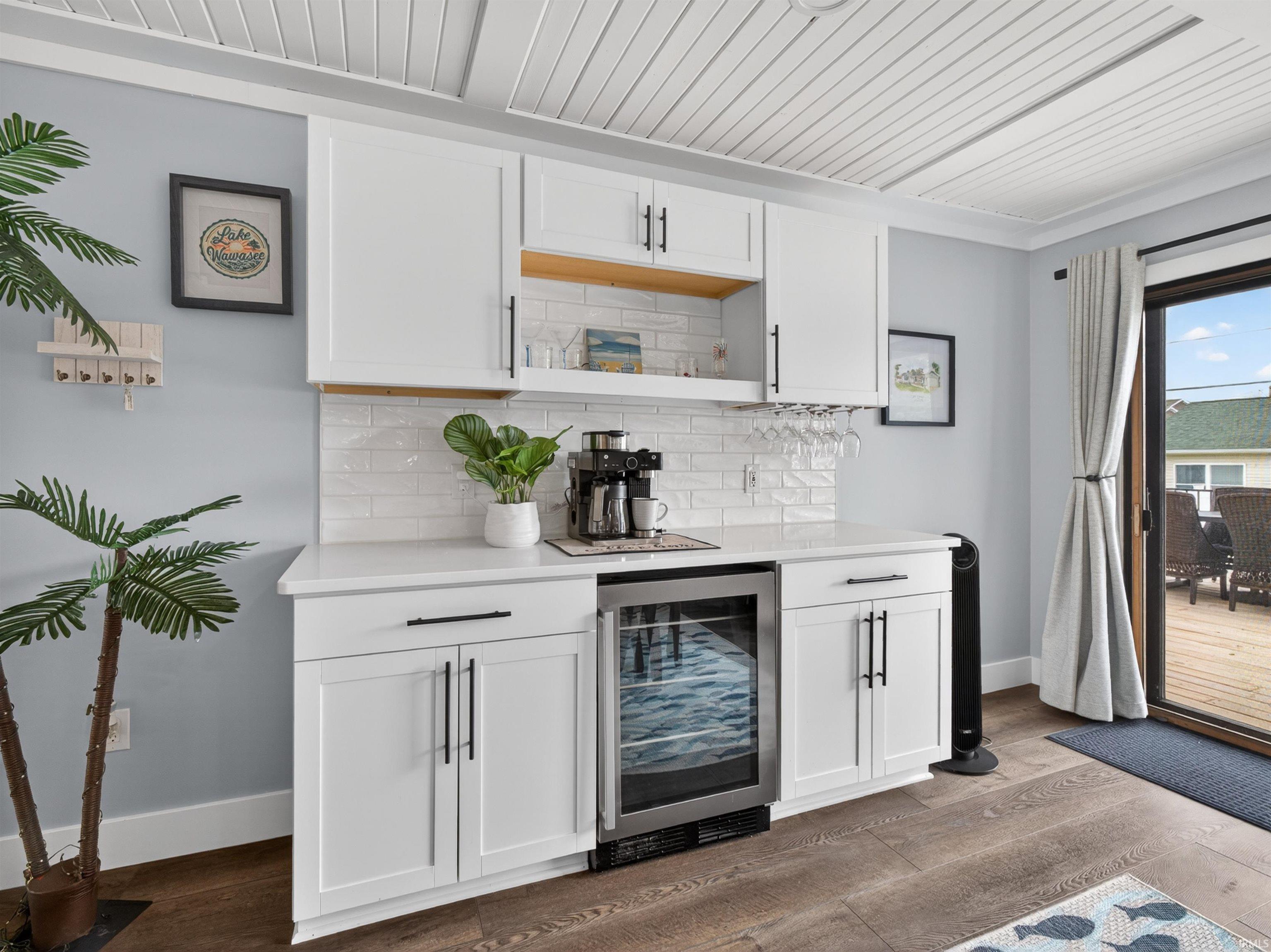 Built-in beverage station featuring white cabinetry, quartz countertops, a subway tile backsplash, and wood-finish flooring