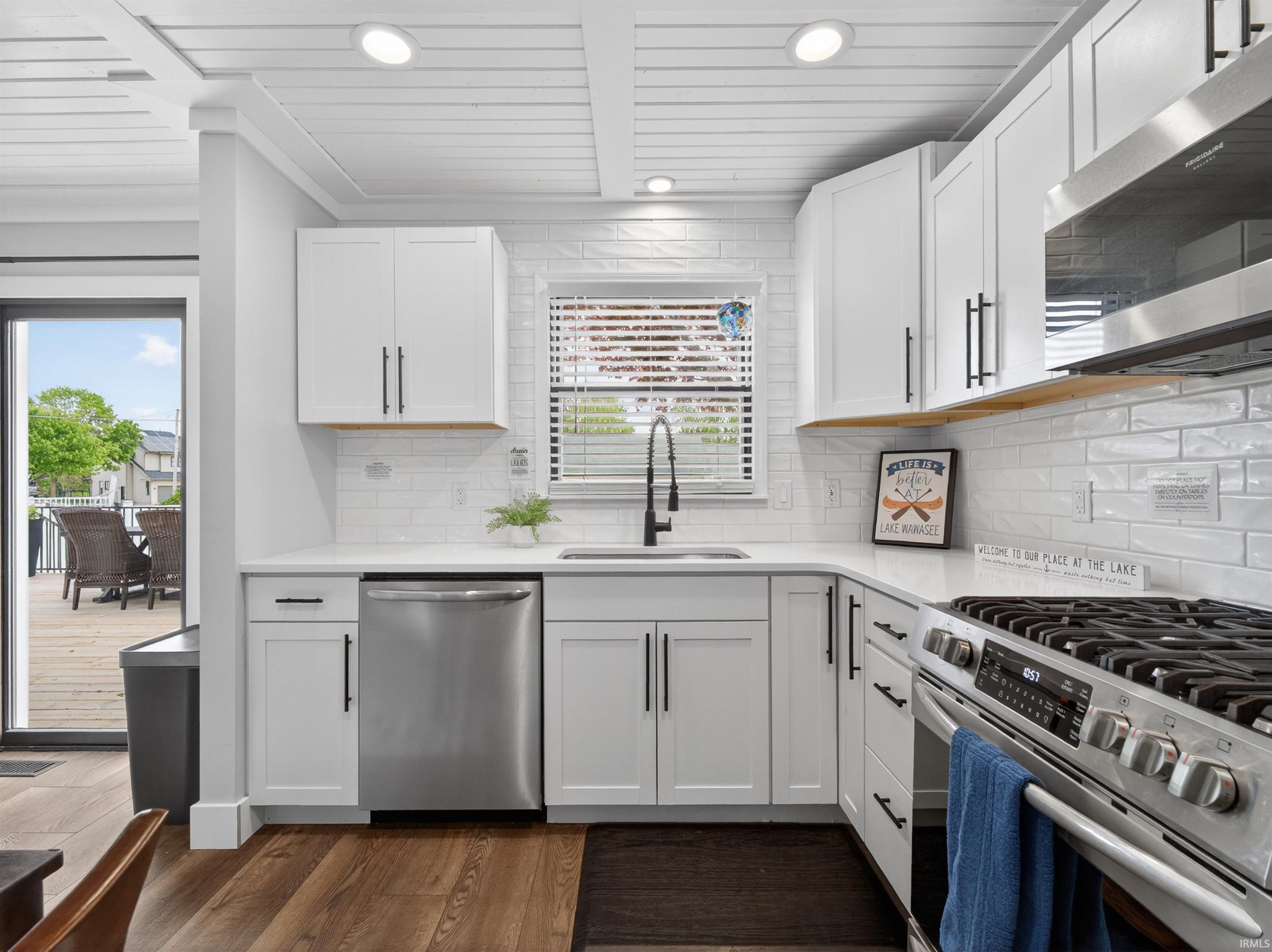 Modern kitchen featuring white shaker cabinetry, stainless steel appliances, white subway tile backsplash, light countertops, and wood-finish flooring