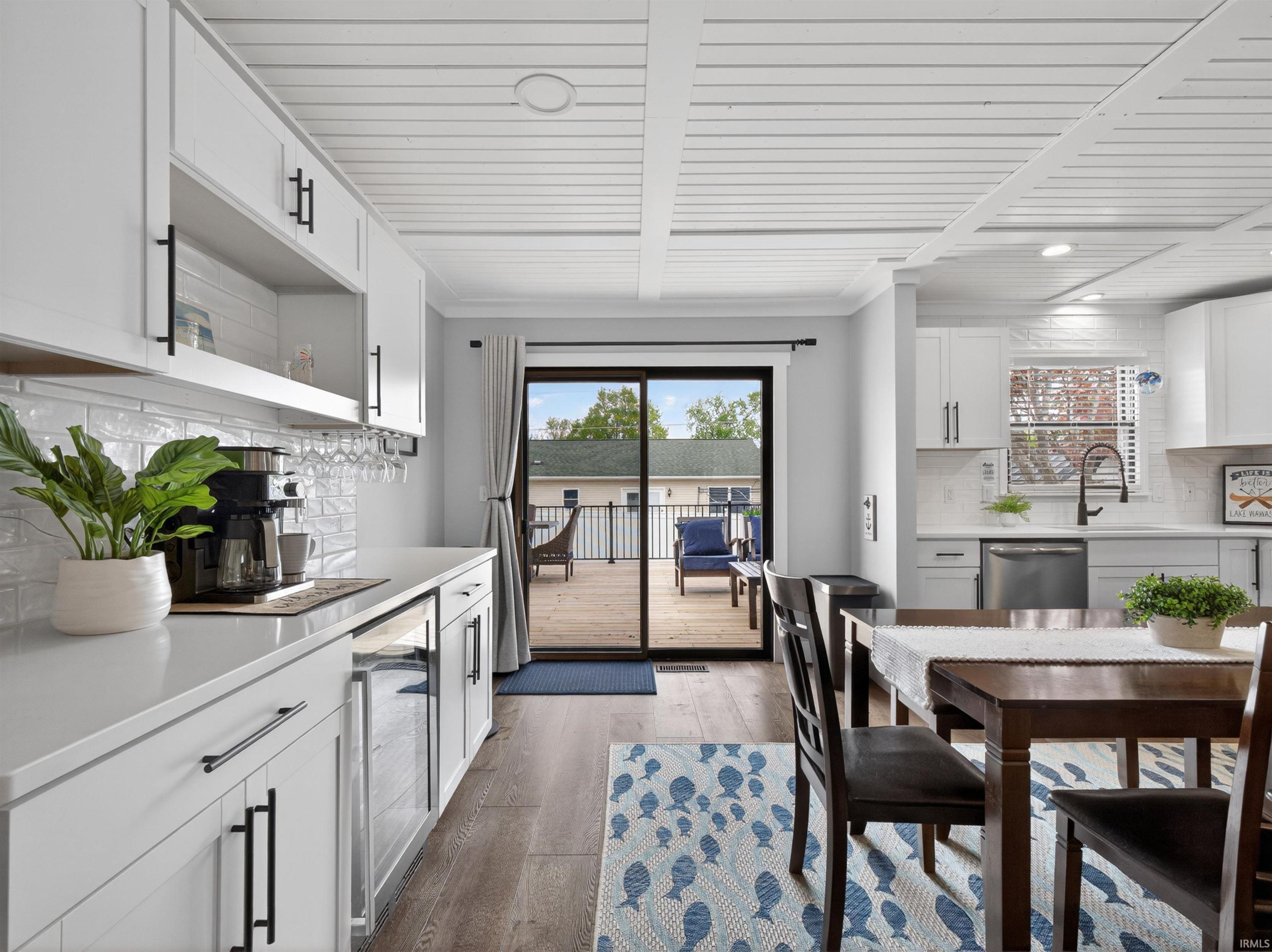 Open-concept kitchen and dining area featuring white shaker-style cabinetry, a subway tile backsplash, dark wood-finish flooring, and direct access to an outdoor deck through a sliding glass door