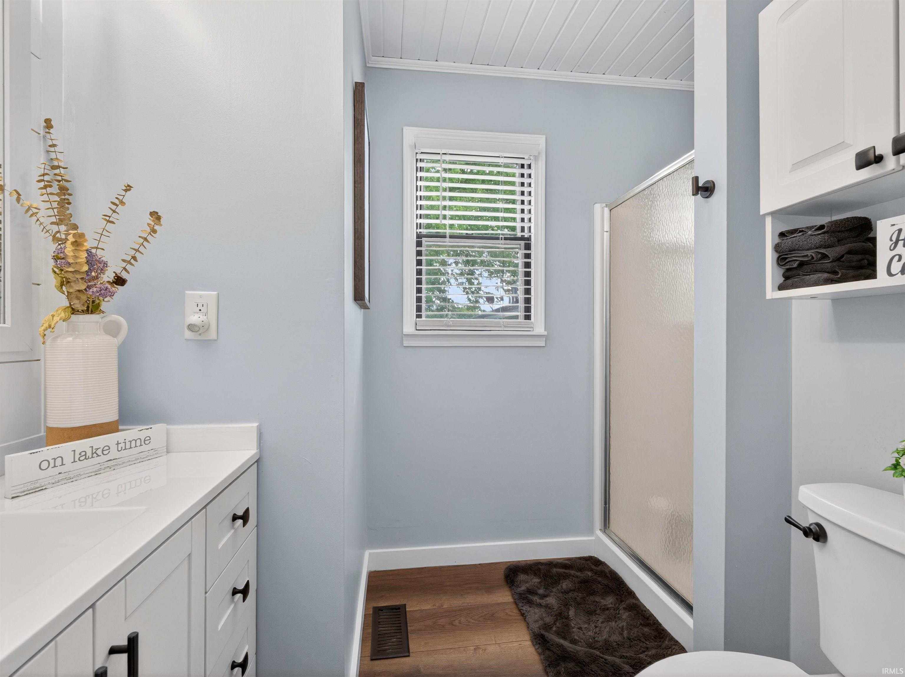 Bathroom featuring a glass-enclosed shower, white vanity with storage, white countertop, and wood-finish flooring
