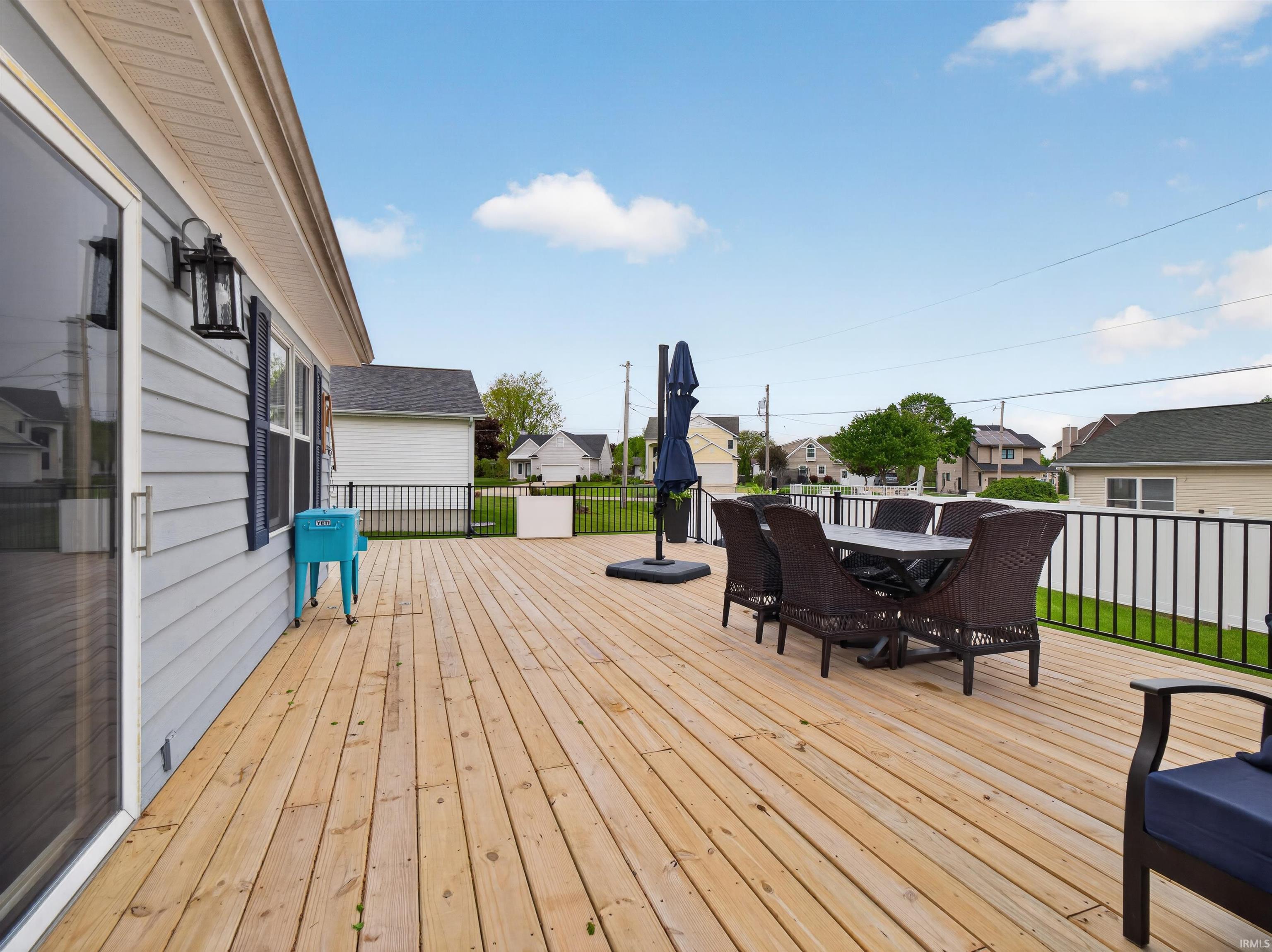 Expansive wood deck with black metal railings, a sliding glass door entry, and light blue siding