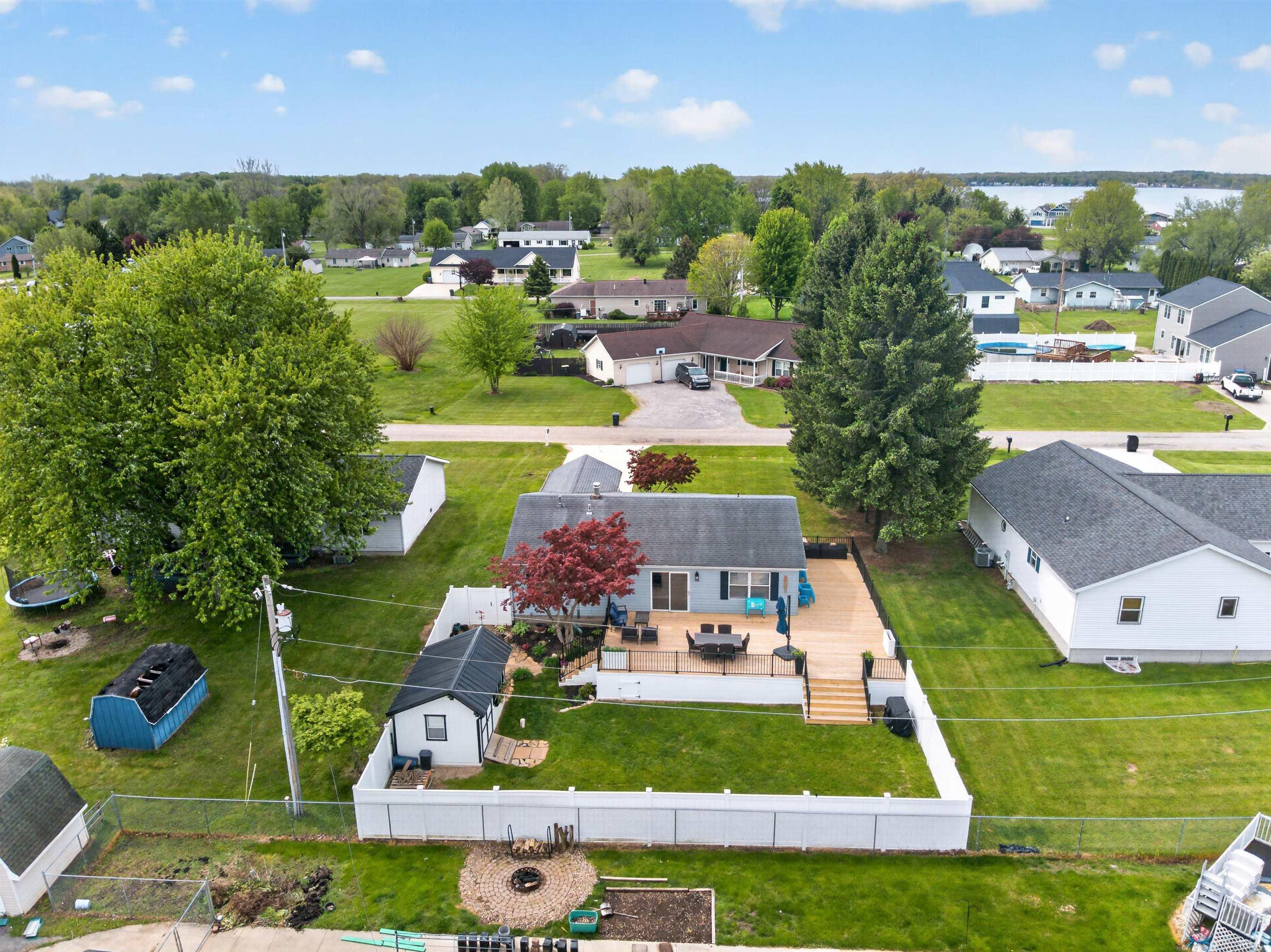 Rear exterior featuring a spacious wood-finish deck with stairs to the lawn, a white privacy fence, and a detached shed