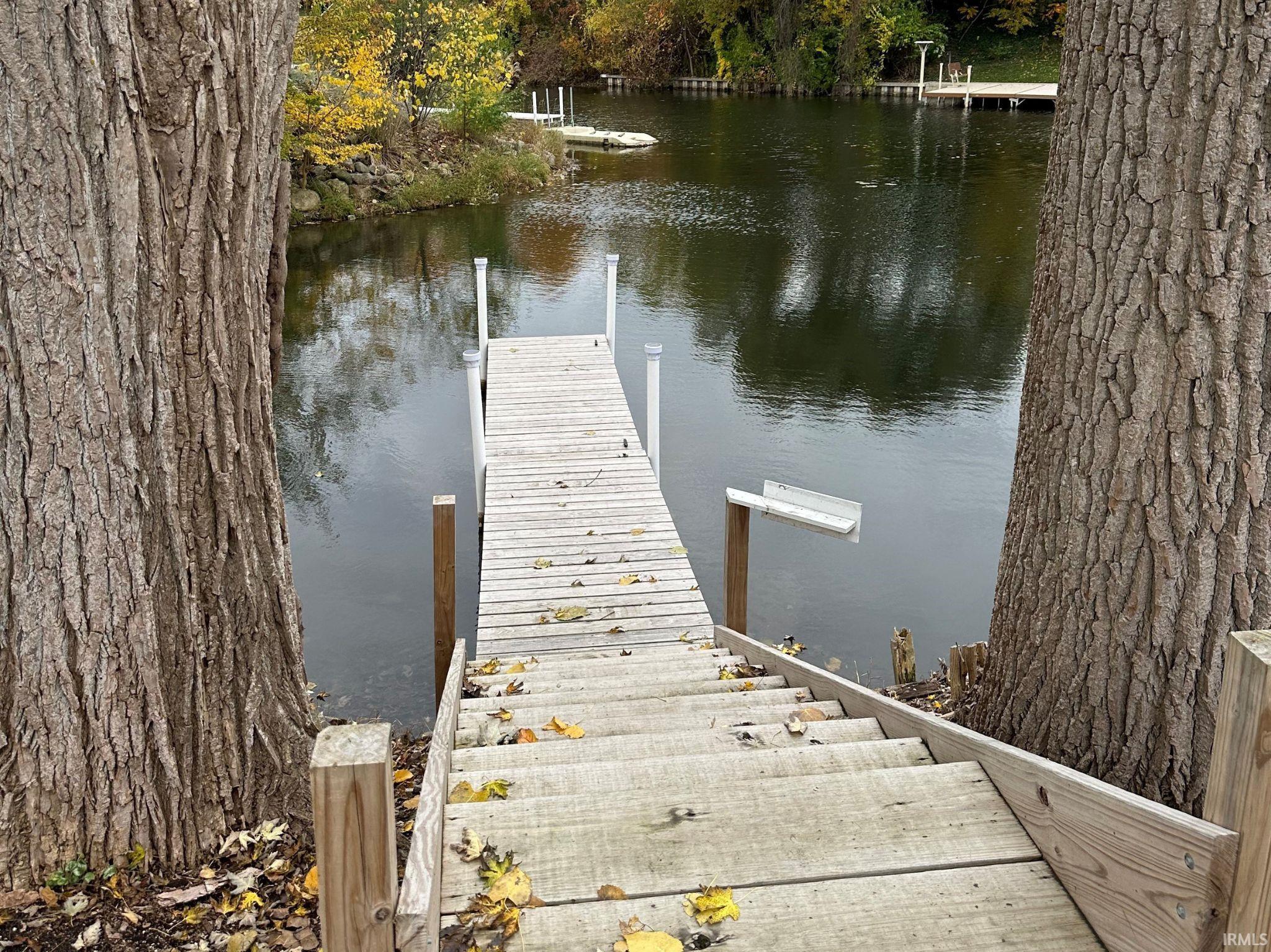 Wood dock extending into calm waters, framed by mature trees