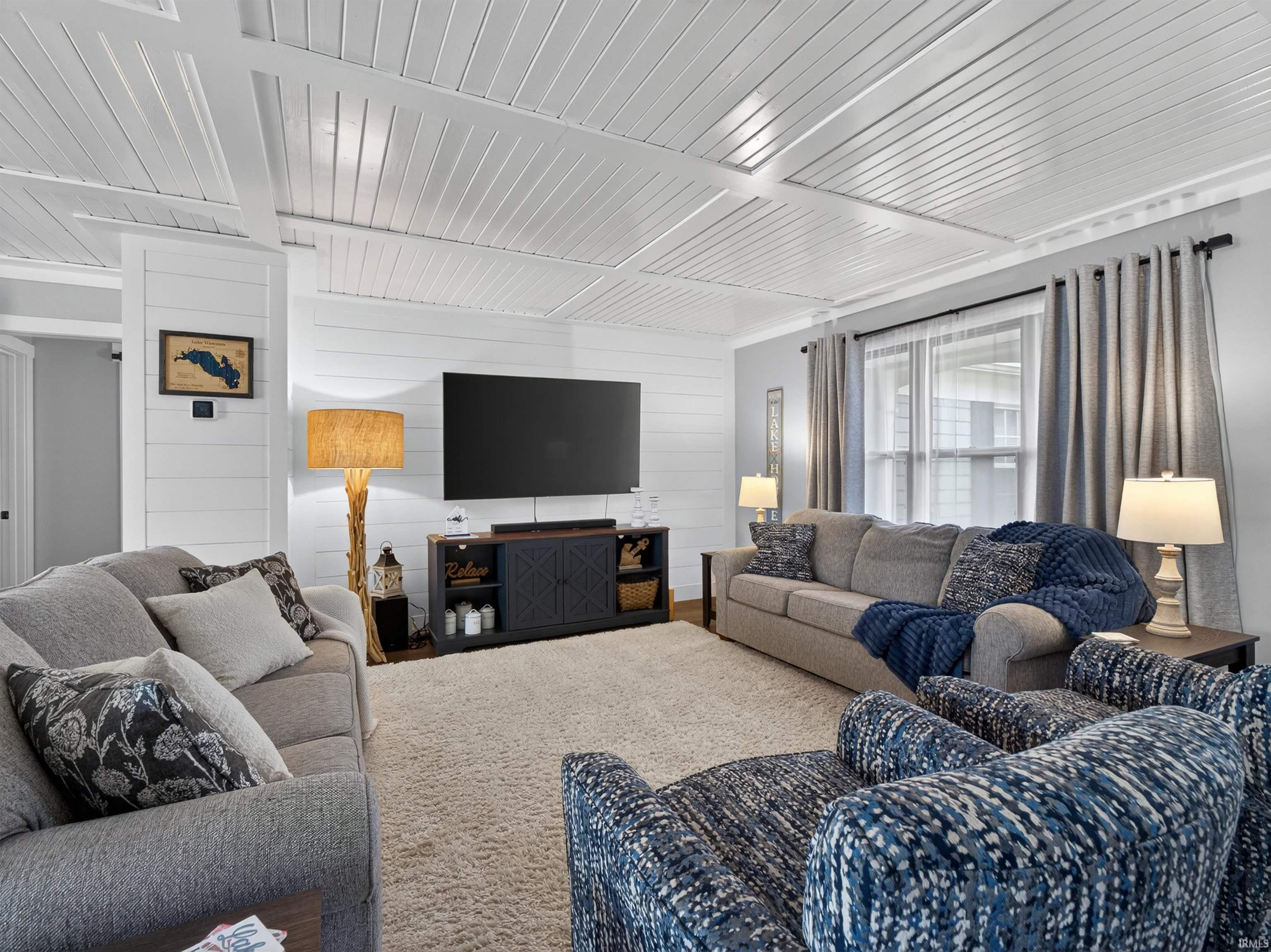 Spacious room featuring white shiplap walls, coffered ceiling, and light-toned carpeting