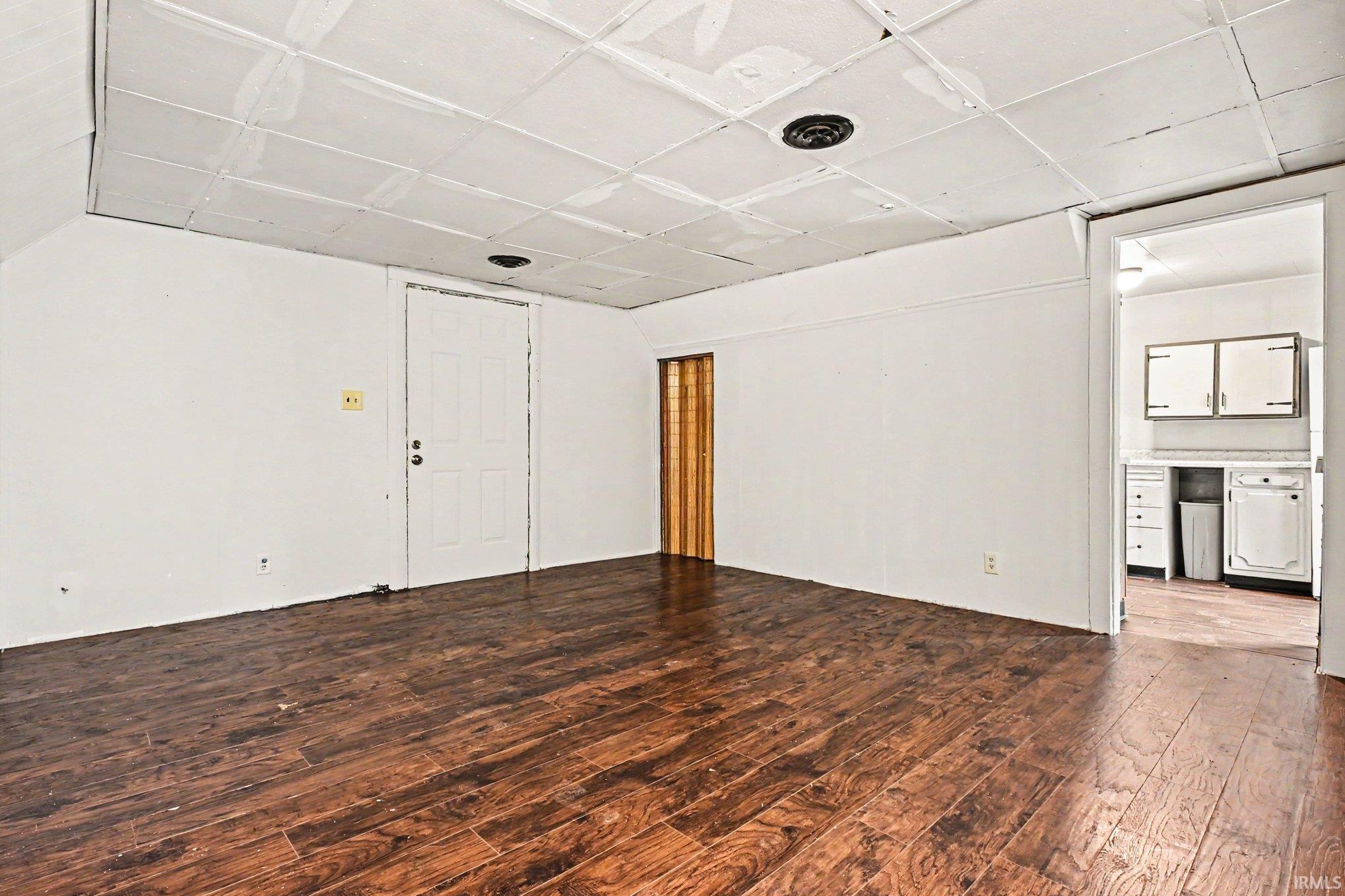 Spacious room featuring wood-finish flooring, white walls, a white paneled door, and a textured ceiling