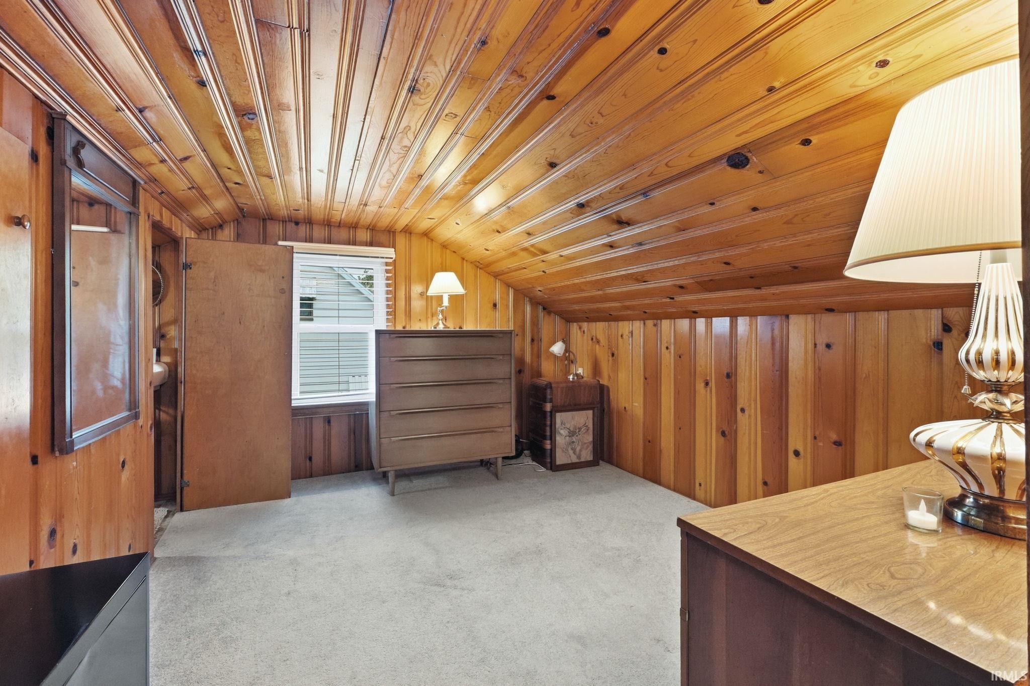Sloped wood-paneled ceiling and walls define this room with light carpeting