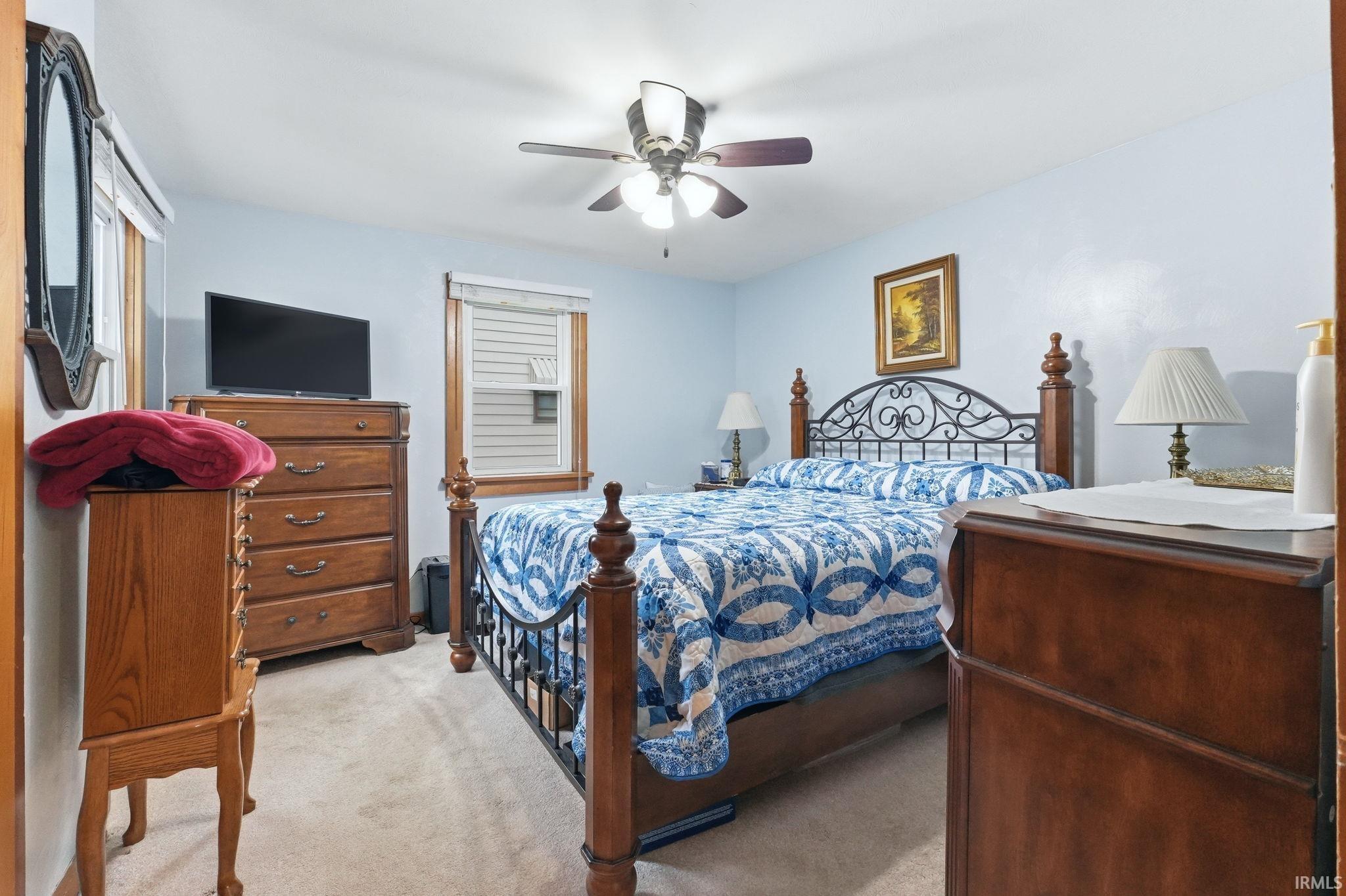 Bedroom featuring light blue walls, wood-trimmed windows with blinds, a ceiling fan with integrated lighting, and neutral-toned carpeting