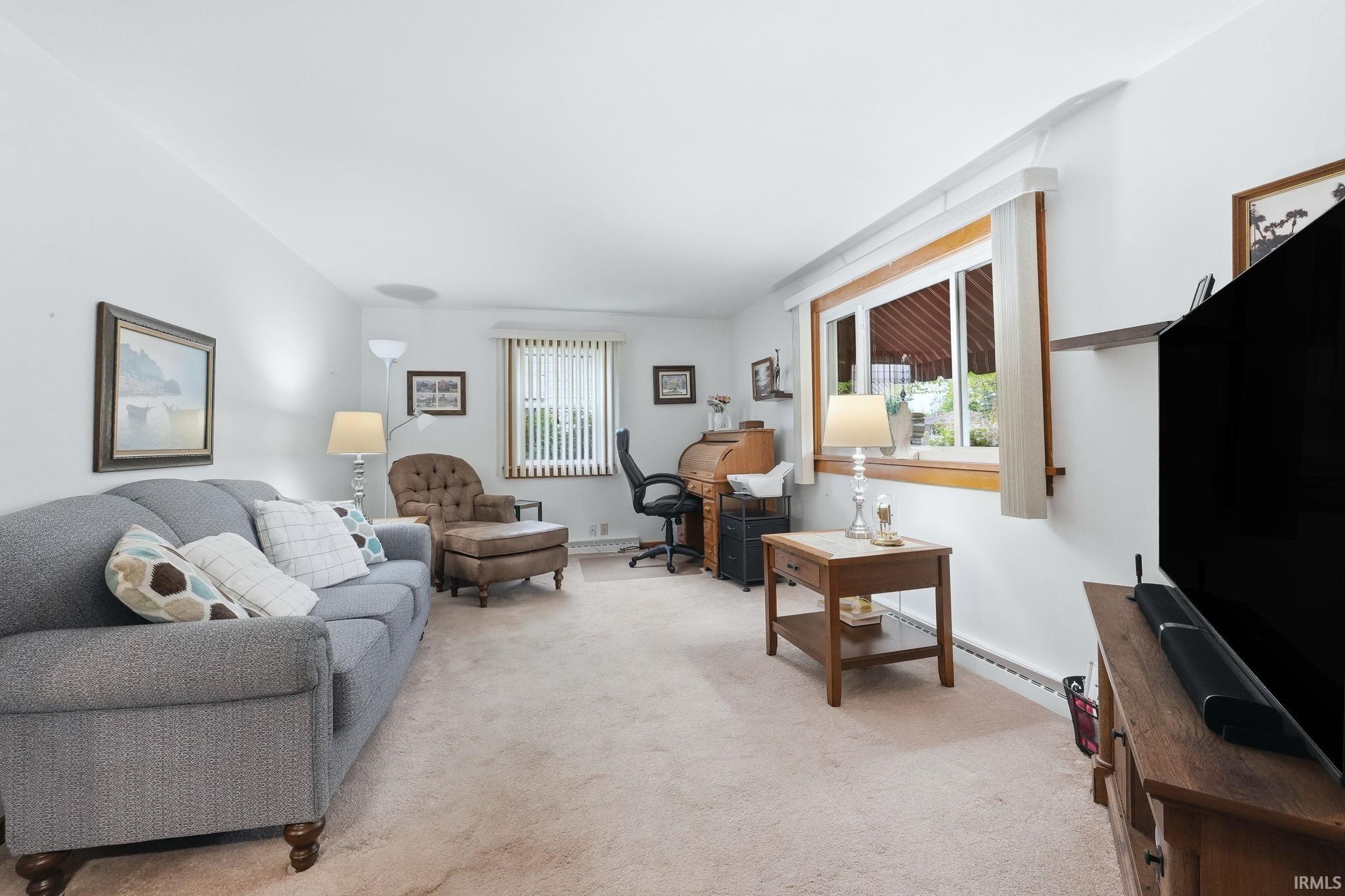 Light-filled living area featuring neutral carpeting, white walls, and a large window with natural wood trim